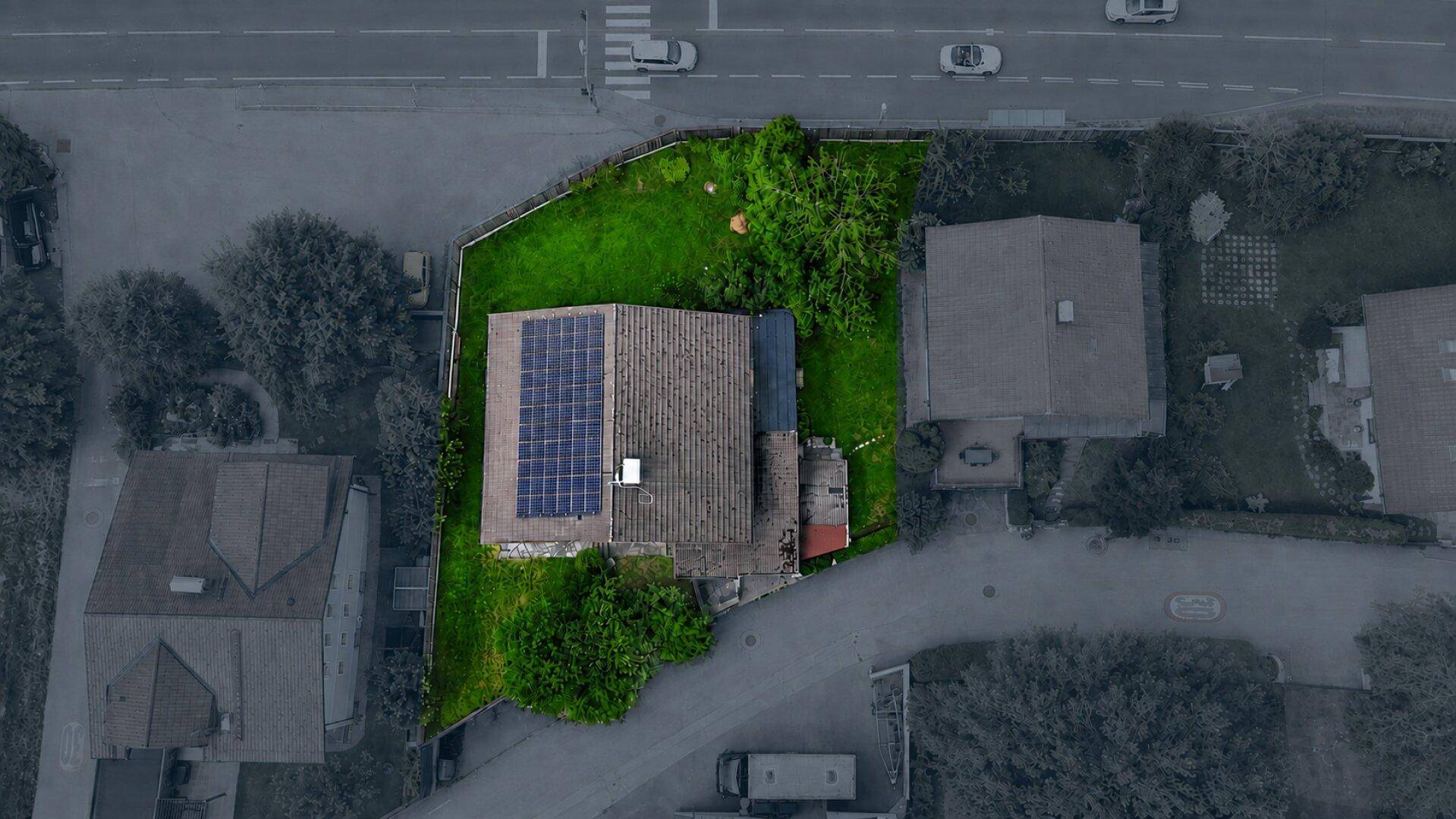 Luftaufnahme des Hauses mit Photovoltaikanlage auf dem Dach und grünem Gartenbereich, umgeben von Straßen.