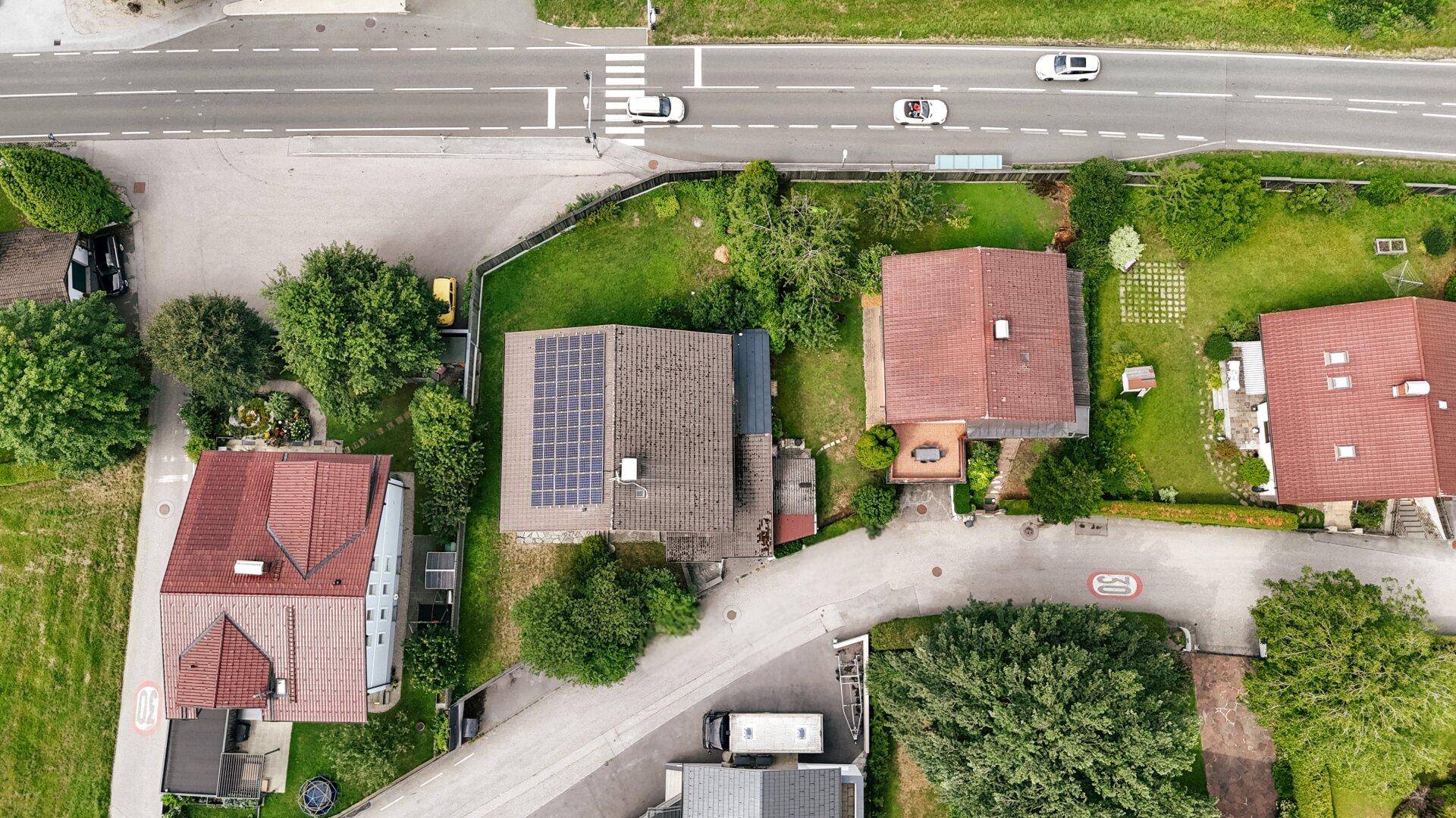 Vogelperspektive des Hauses mit Photovoltaikanlage auf dem Dach, umgeben von grünem Garten und Straßen.