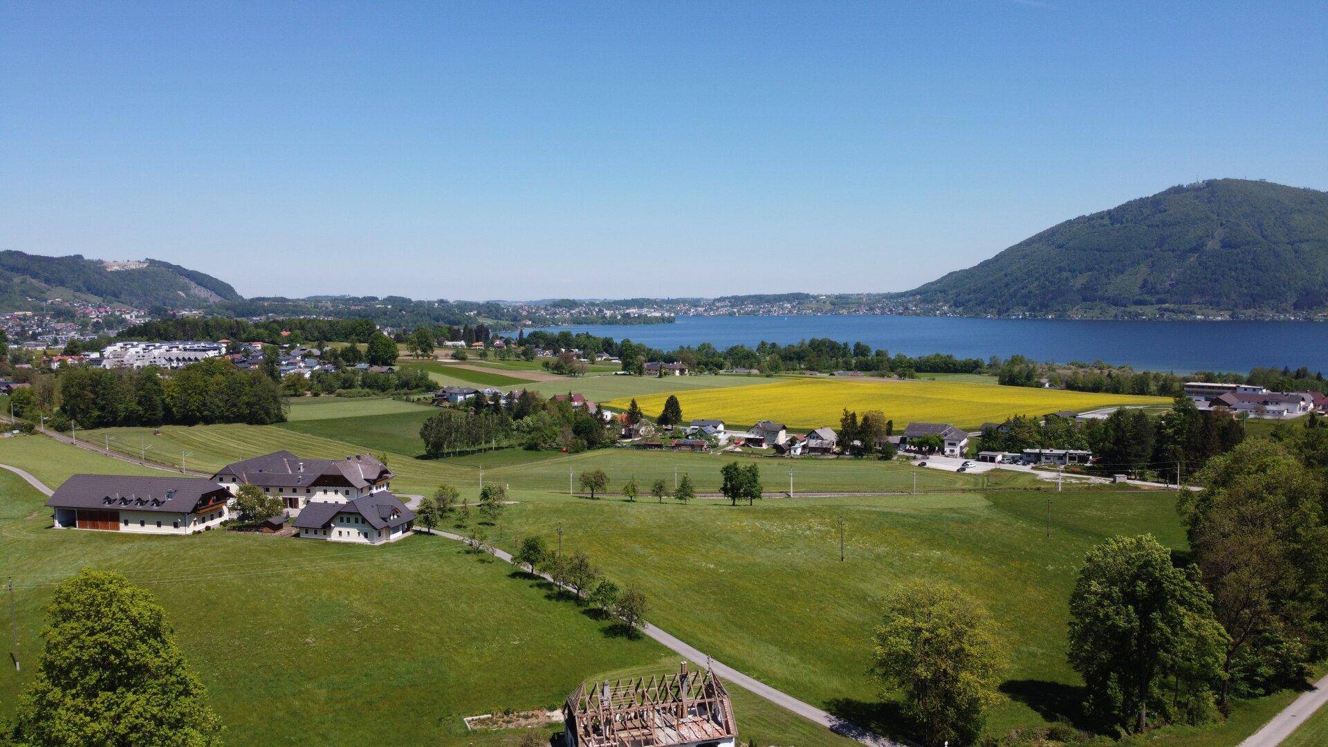 Idyllische Landschaft mit einem See, Bergen und weiten grünen Feldern unter blauem Himmel.