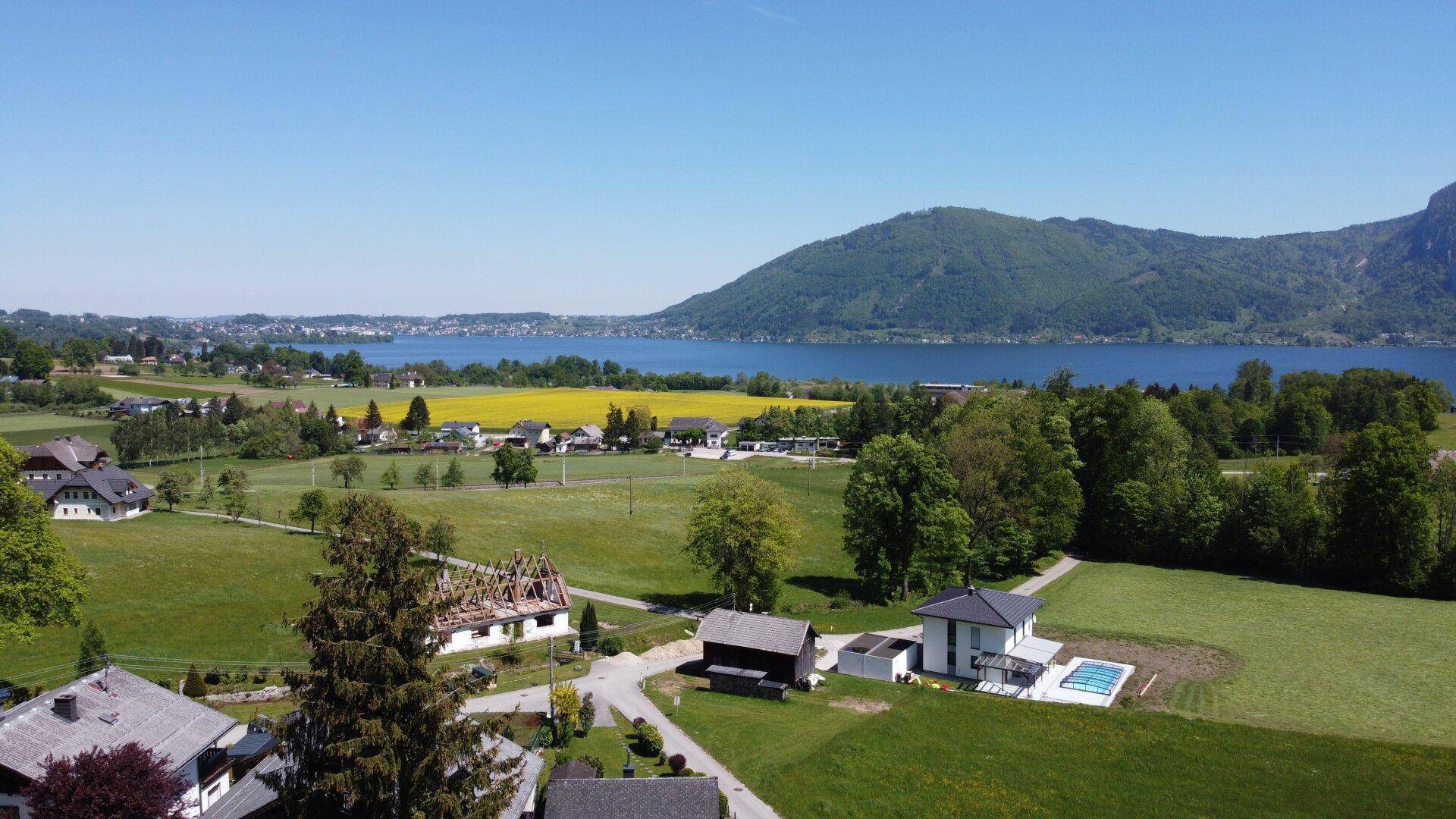 Weitläufige Landschaft mit See und Bergen, umgeben von grünen Feldern und vereinzelten Häusern.