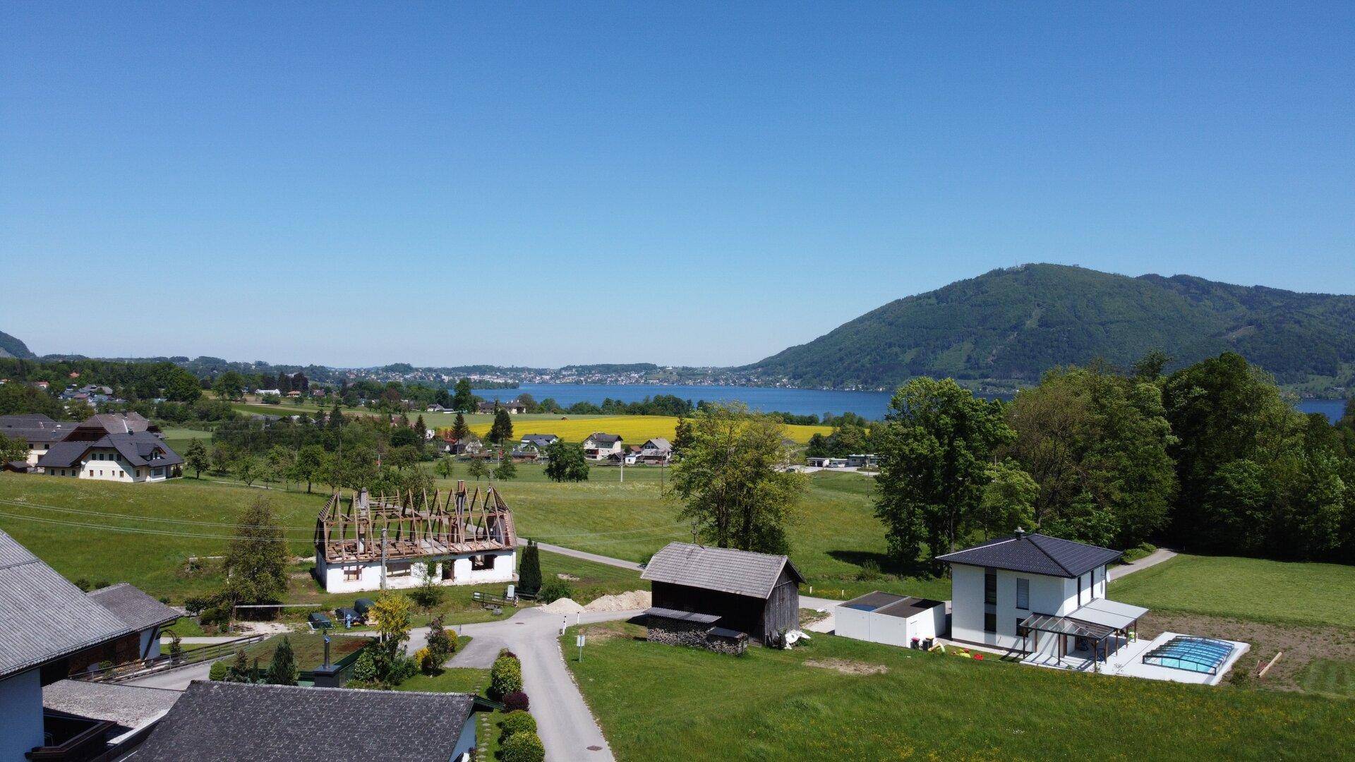 Luftaufnahme einer ländlichen Gegend mit See, Bergen und einem Neubau sowie einem Haus im Bau.