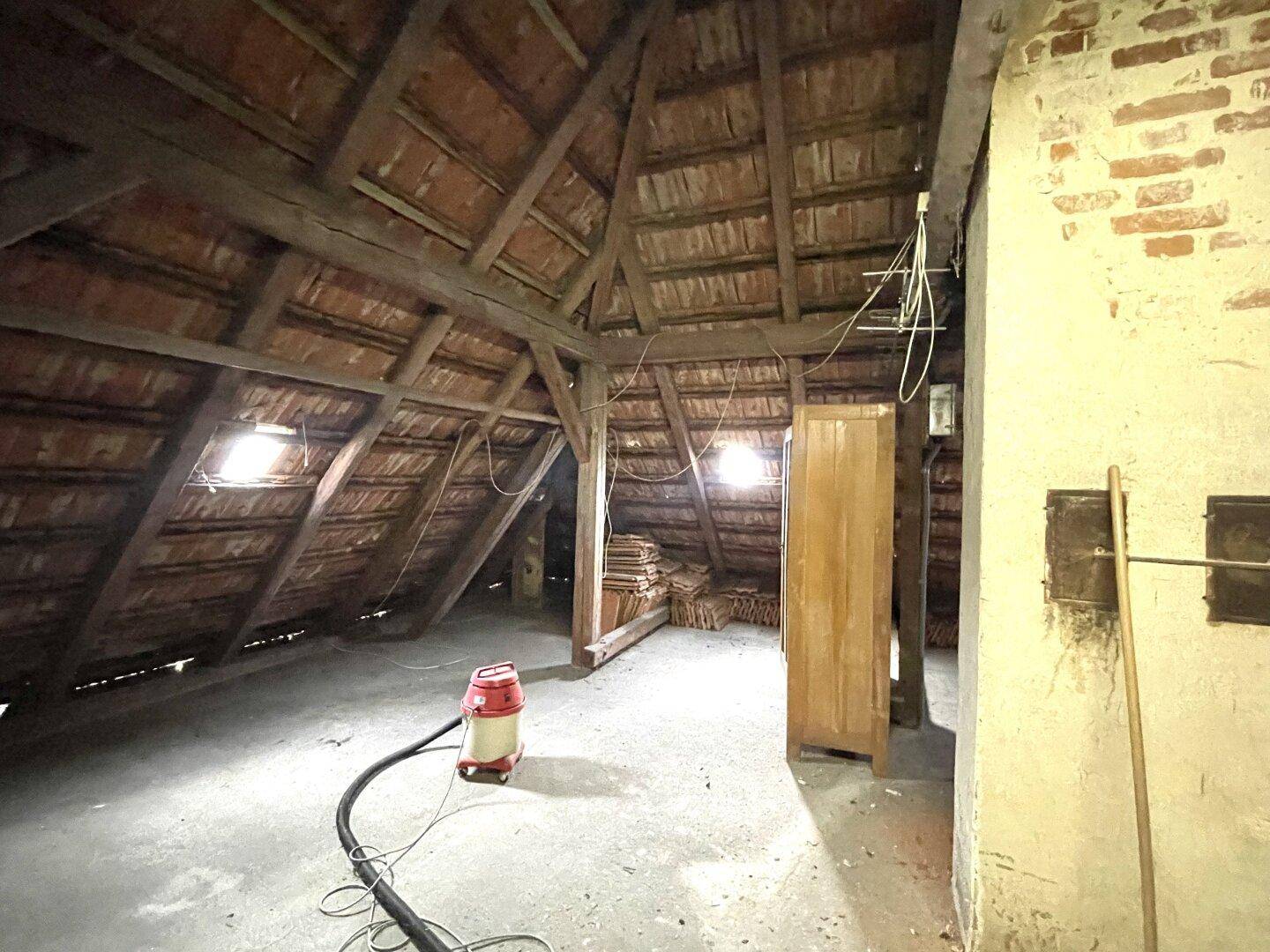 Geräumiger Dachboden mit sichtbaren Holzbalken und Ziegeln, der als Lagerraum dient.