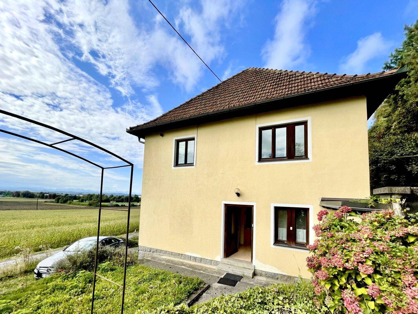 Gelbes Einfamilienhaus mit braunem Ziegeldach und Blick auf weite Felder unter blauem Himmel.