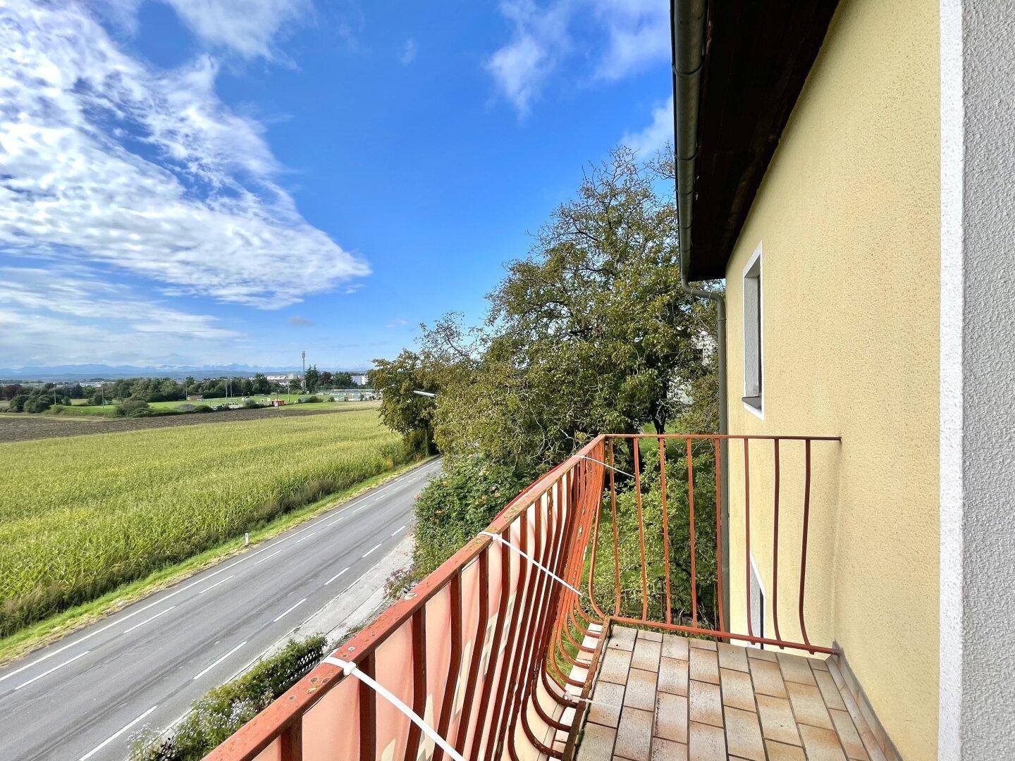 Kleiner Balkon mit rotem Geländer bietet einen weiten Blick über die Straße und grüne Felder.