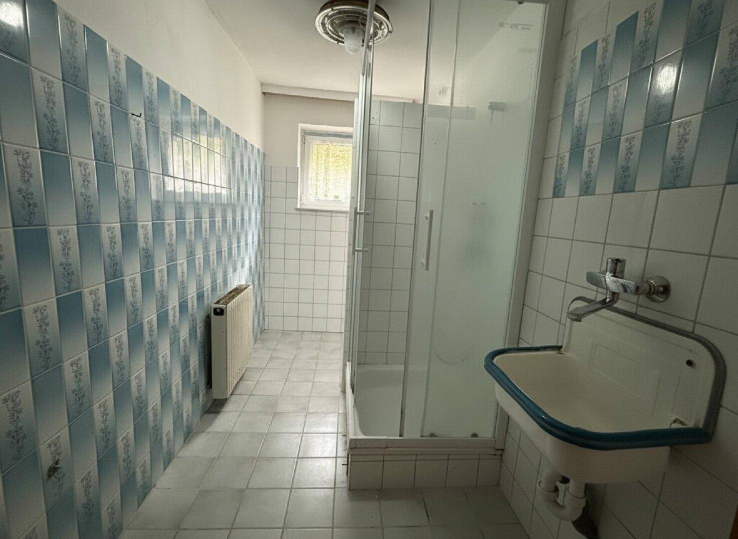 Badezimmer im Stil der 80er Jahre mit blauen und weißen Fliesen, Dusche und Fenster.