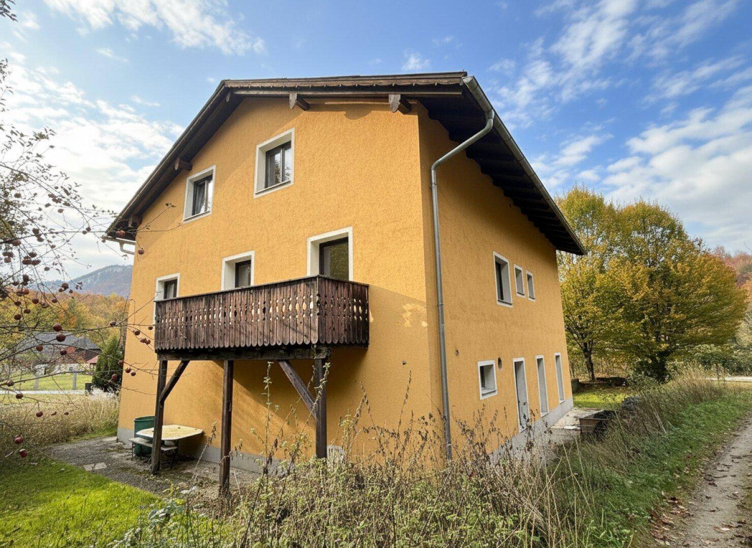 Seitenansicht des Hauses mit einem Holzbalkon und Blick auf die umliegende Natur und Obstbäume.