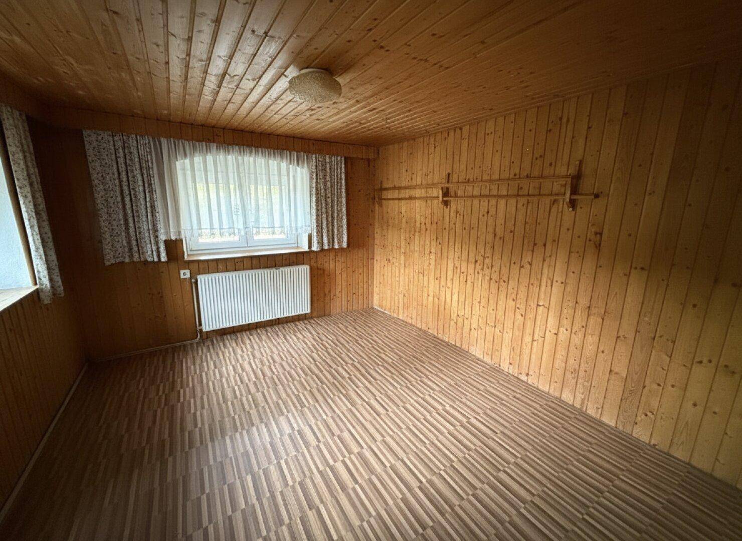 Schlafzimmer mit Holztäfelung an Wänden und Decke sowie einem Fenster mit Blick ins Grüne.