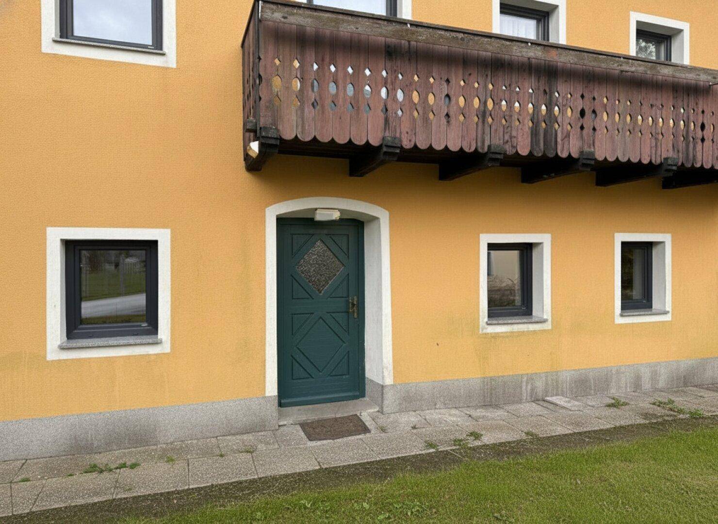 Eingangsbereich des Hauses mit einer grünen Holztür und einem darüberliegenden Balkon.