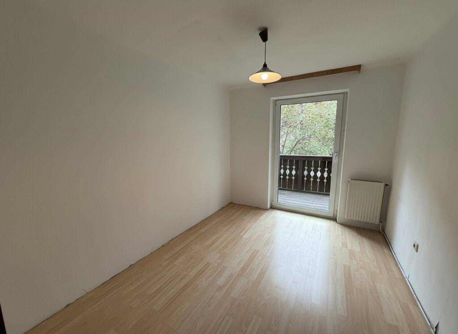 Helles Zimmer mit Laminatboden und direktem Zugang zu einem Balkon mit Holzbalkongeländer.