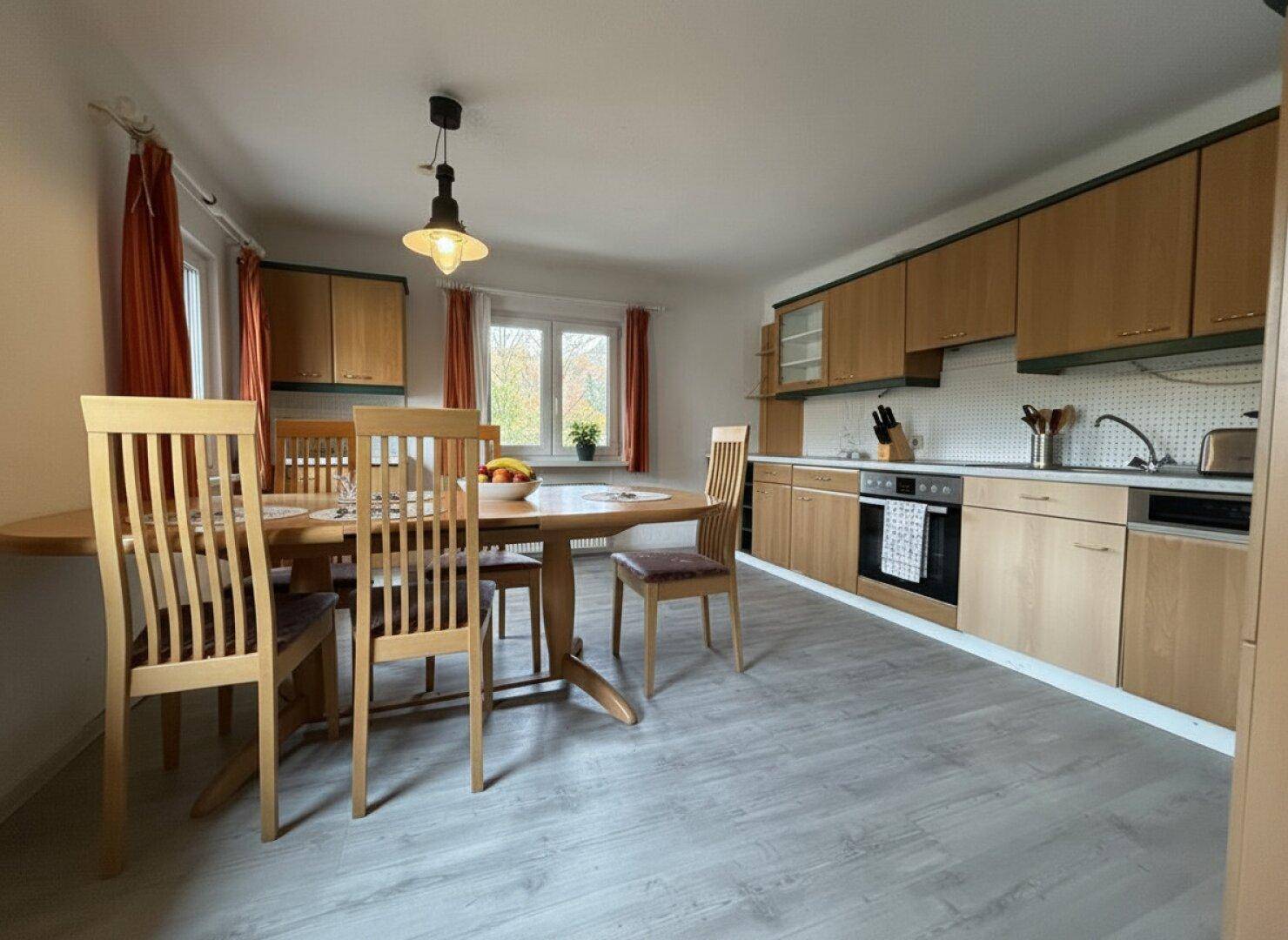 Geräumige Wohnküche mit Holzeinbauten, Essbereich und Blick auf die herbstliche Landschaft.