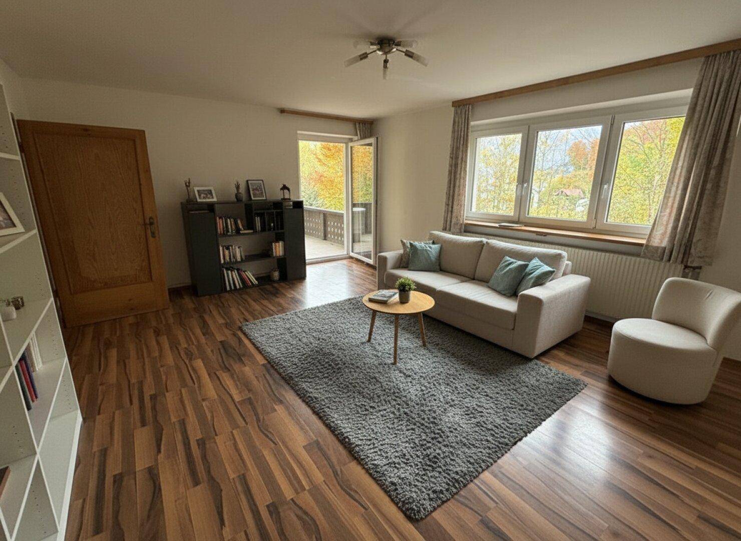 Wohnzimmer mit dunklem Laminatboden, beigem Sofa und Zugang zu einem sonnigen Balkon.