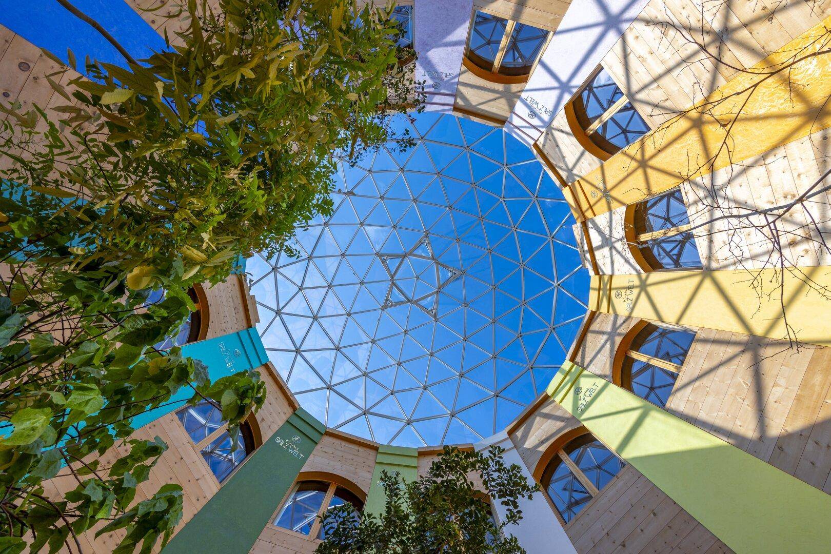 Beeindruckende Glaskuppel über einem hellen Atrium mit farbigen Wänden und Pflanzen.