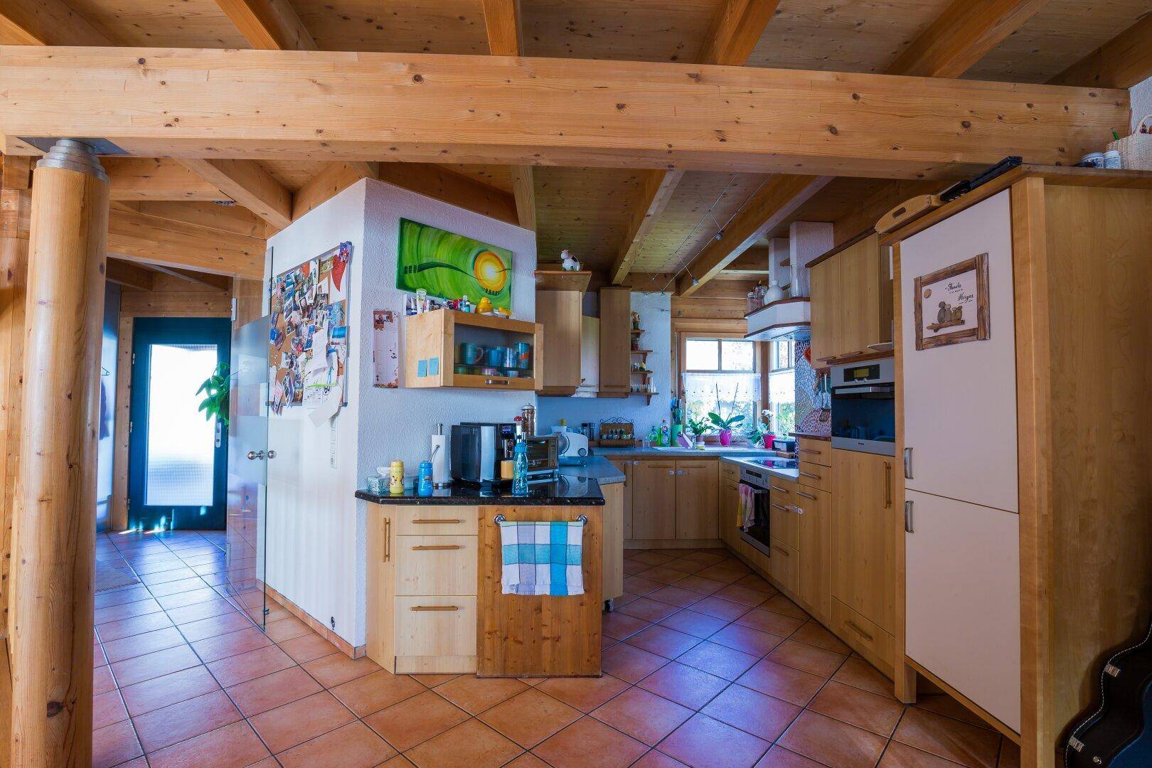 Rustikale Küche mit Holzschränken, dunkler Arbeitsplatte und Terrakottafliesen, offen zum Wohnbereich.