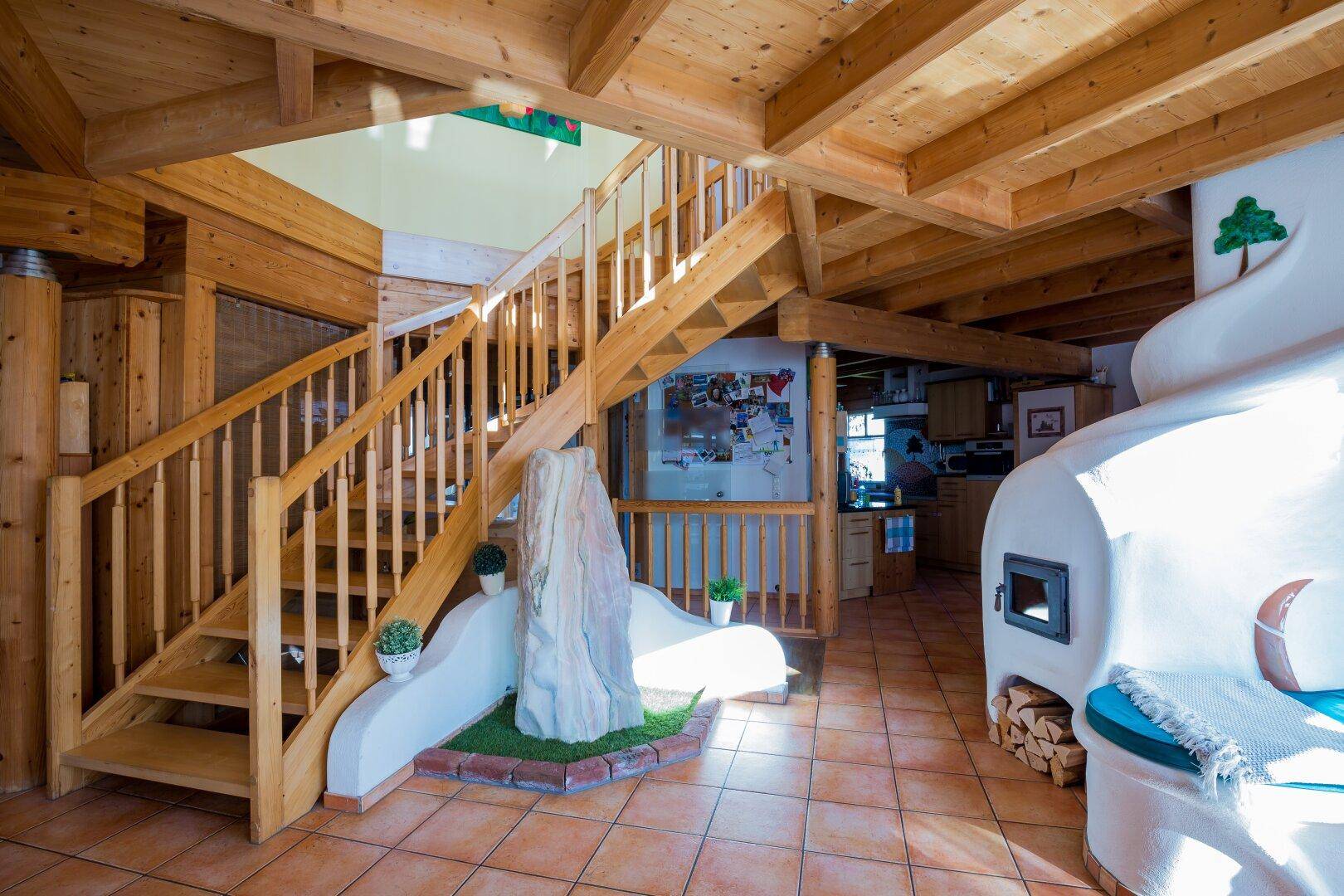 Gemütlicher Wohnbereich mit Kachelofen, Holztreppe und Terrakottafliesen, der eine warme Atmosphäre schafft.