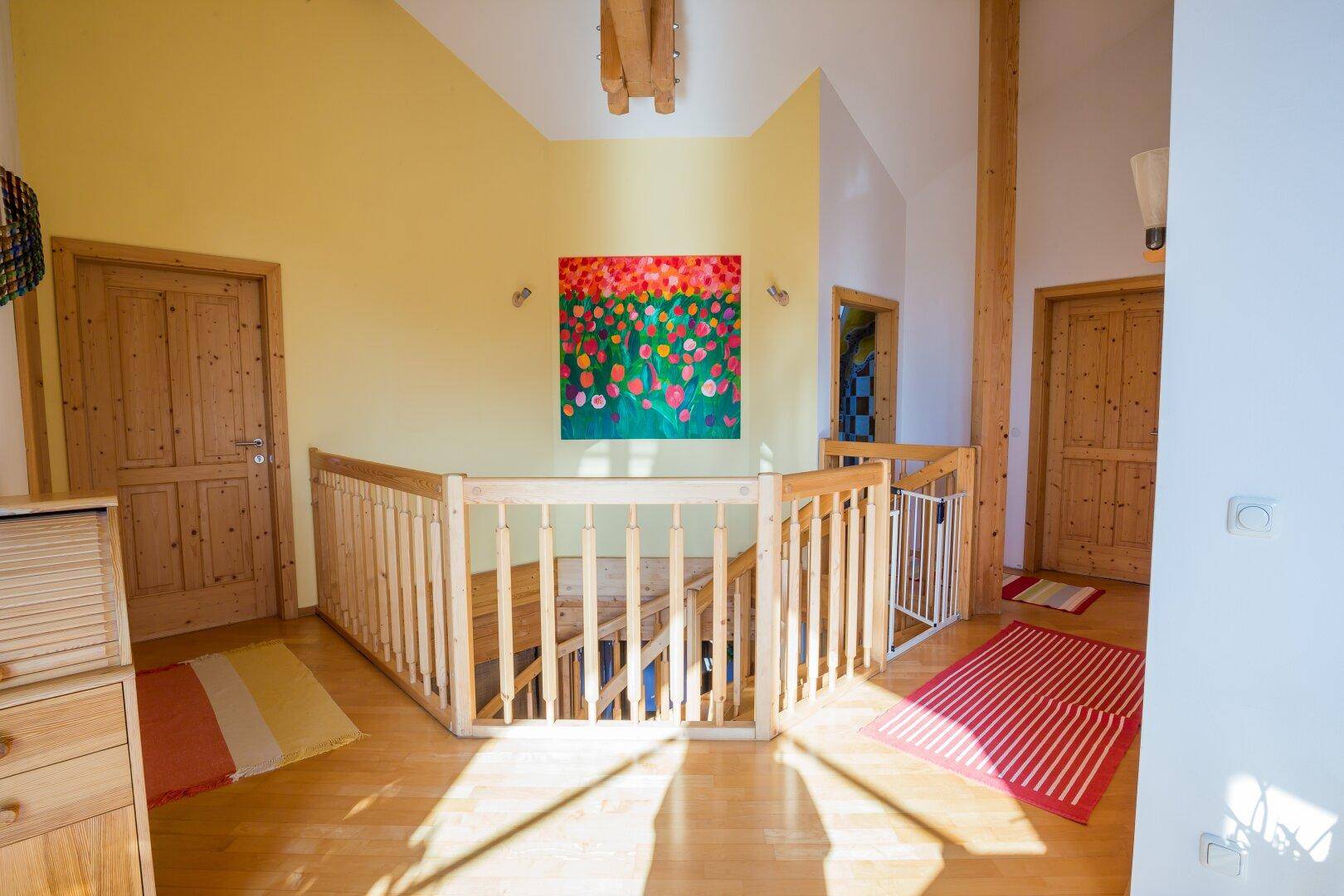Obergeschoss-Flur mit Holzgeländer, Holzboden und farbenfrohem Wandbild, der zu den Zimmern führt.