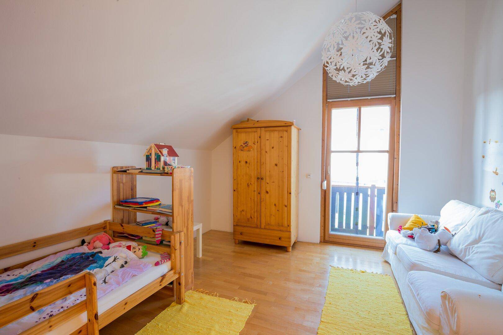 Kinderzimmer mit Holzboden, Dachschräge und Zugang zu einem französischen Balkon.