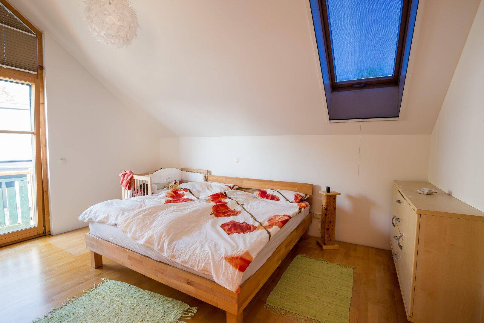 Schlafzimmer mit Holzbett, Holzboden, Dachschräge und Dachfenster für natürliches Licht.
