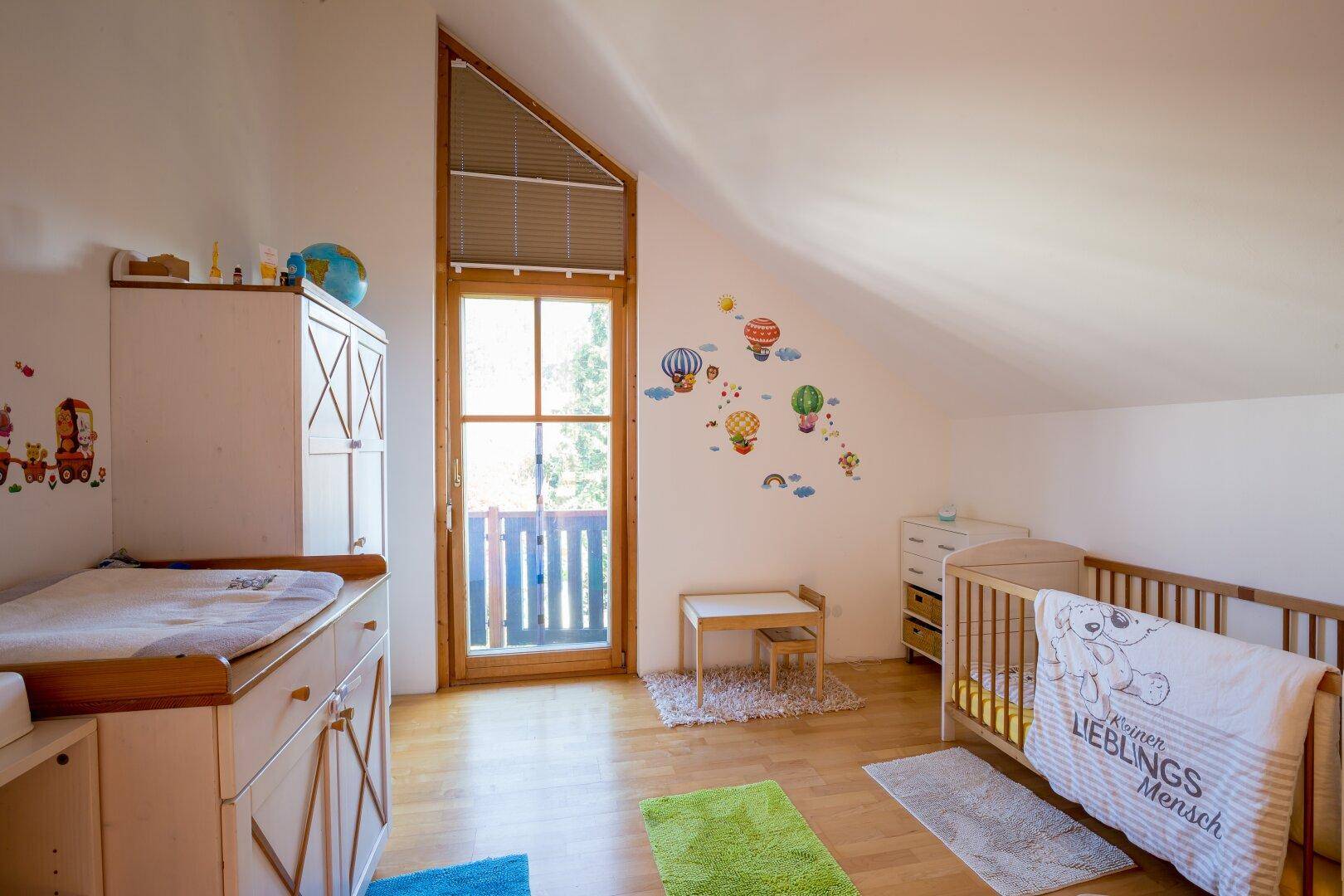 Helles Kinderzimmer mit Wickeltisch, Babybett und Zugang zu einem französischen Balkon.
