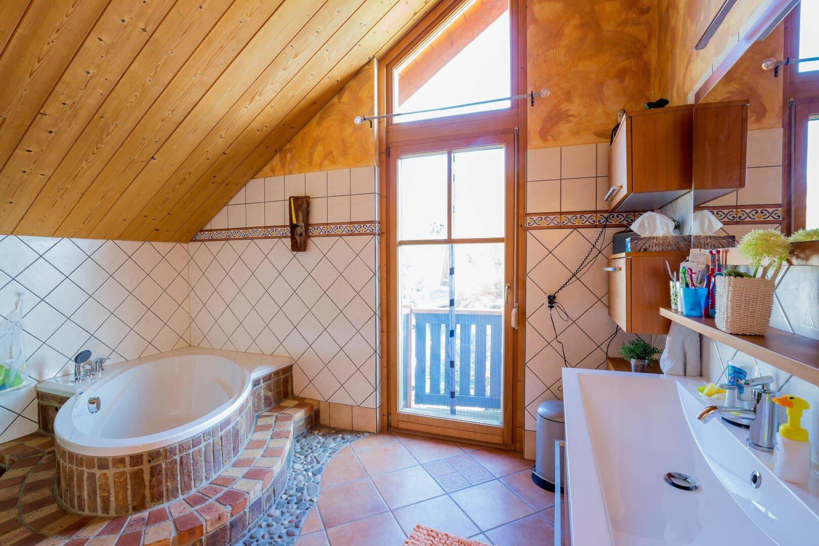 Geräumiges Badezimmer mit Eckbadewanne, Dachschräge und Zugang zu einem französischen Balkon.