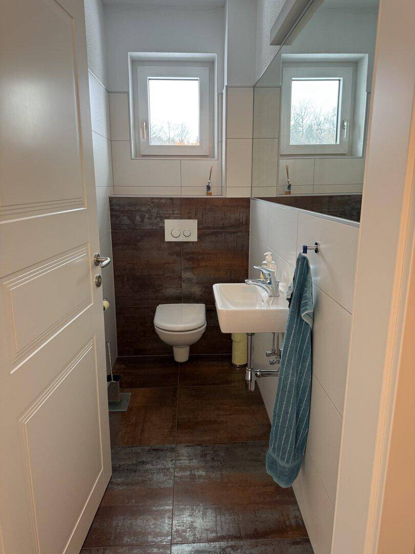 Modernes Gäste-WC mit Wand-WC, kleinem Waschbecken und Fenster für natürliche Belüftung.