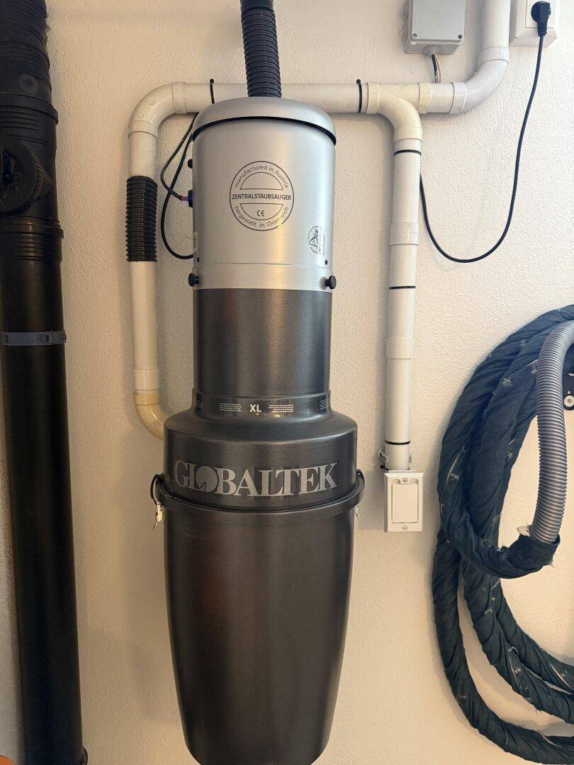Zentralstaubsaugeranlage von Globaltek an der Wand montiert mit sichtbaren Rohren und Anschlüssen.