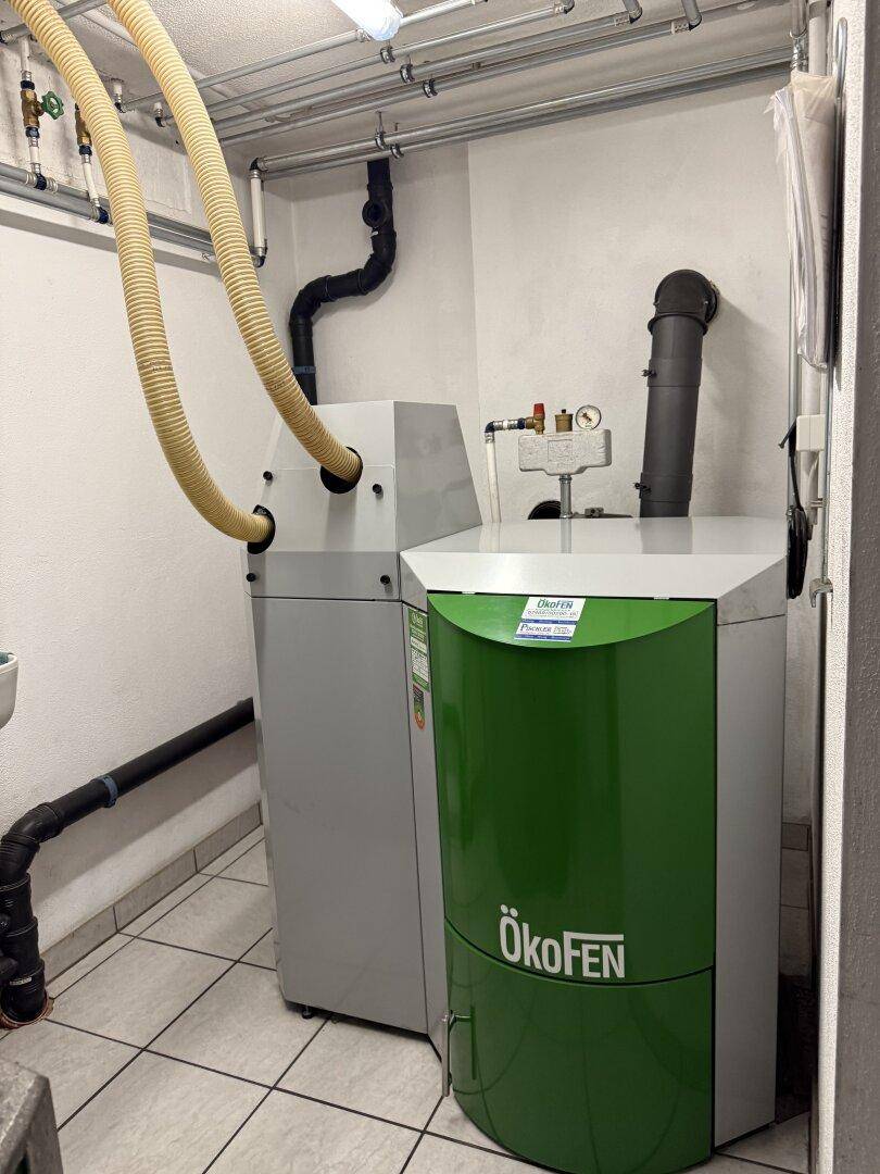 Moderner Pelletkessel von Ökofen in einem Technikraum mit sichtbaren Rohren und Leitungen.