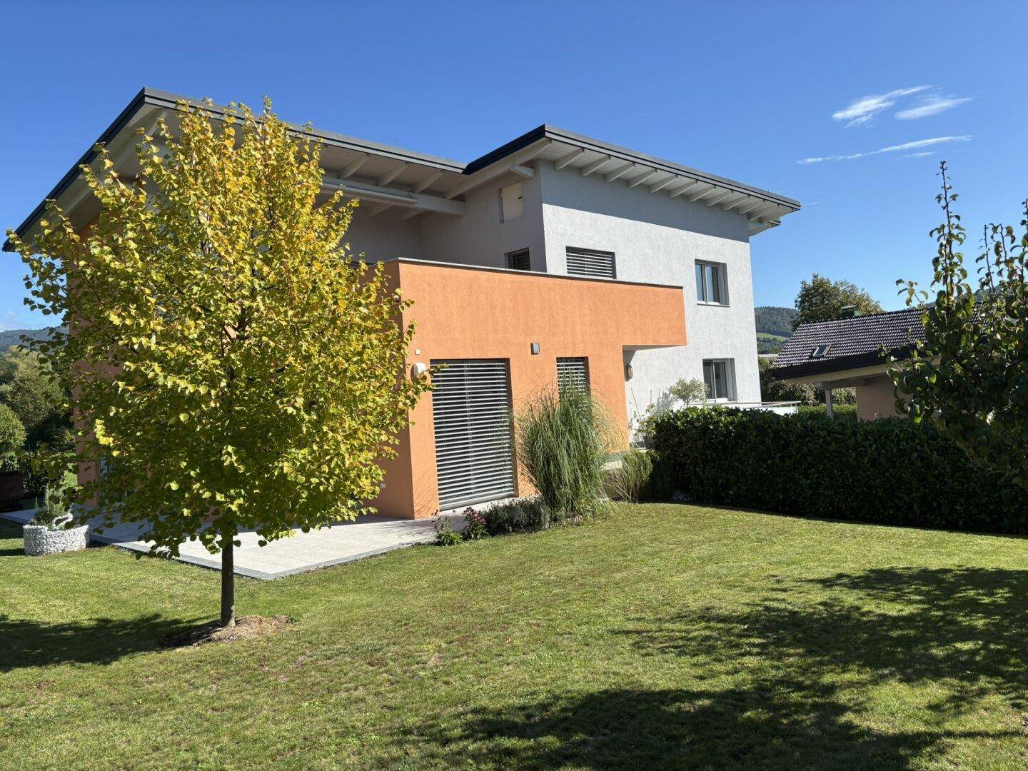 Seitenansicht eines modernen Hauses mit orangefarbenen Akzenten und einem gepflegten Rasen im Vorgarten.