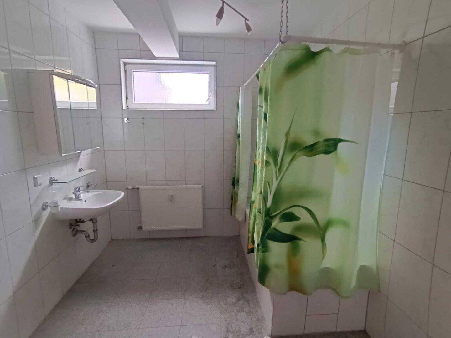 Badezimmer mit Duschvorhang, Waschbecken und Fenster für Tageslicht.