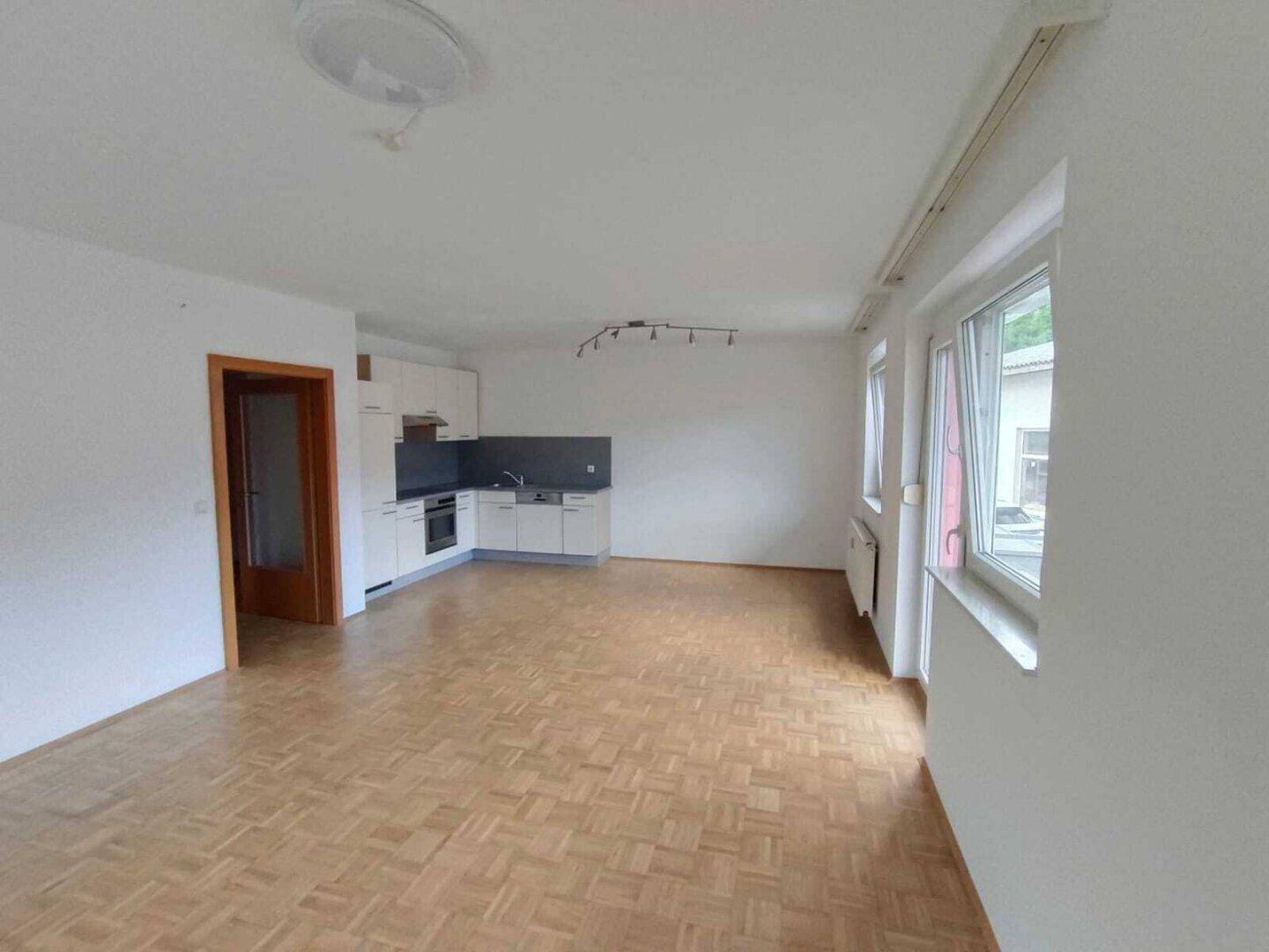 Lichtdurchfluteter Wohnbereich mit integrierter Küchenzeile und Parkettboden.