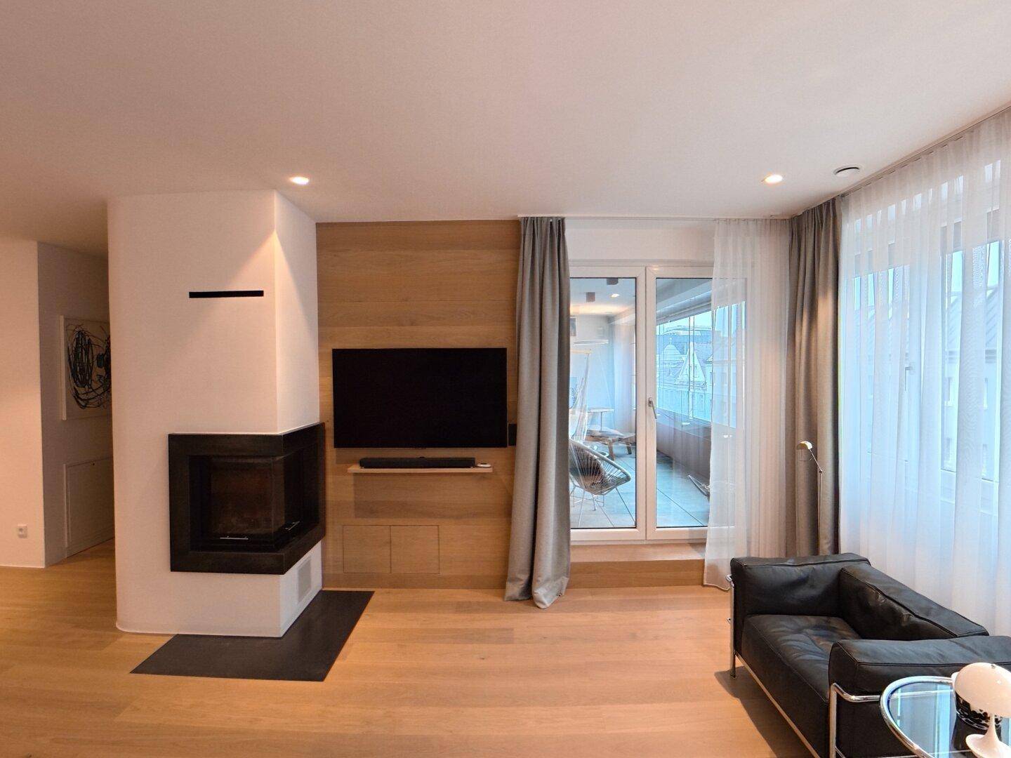 Helles Wohnzimmer mit Kamin, Holzboden und Zugang zu einem Balkon oder einer Terrasse.