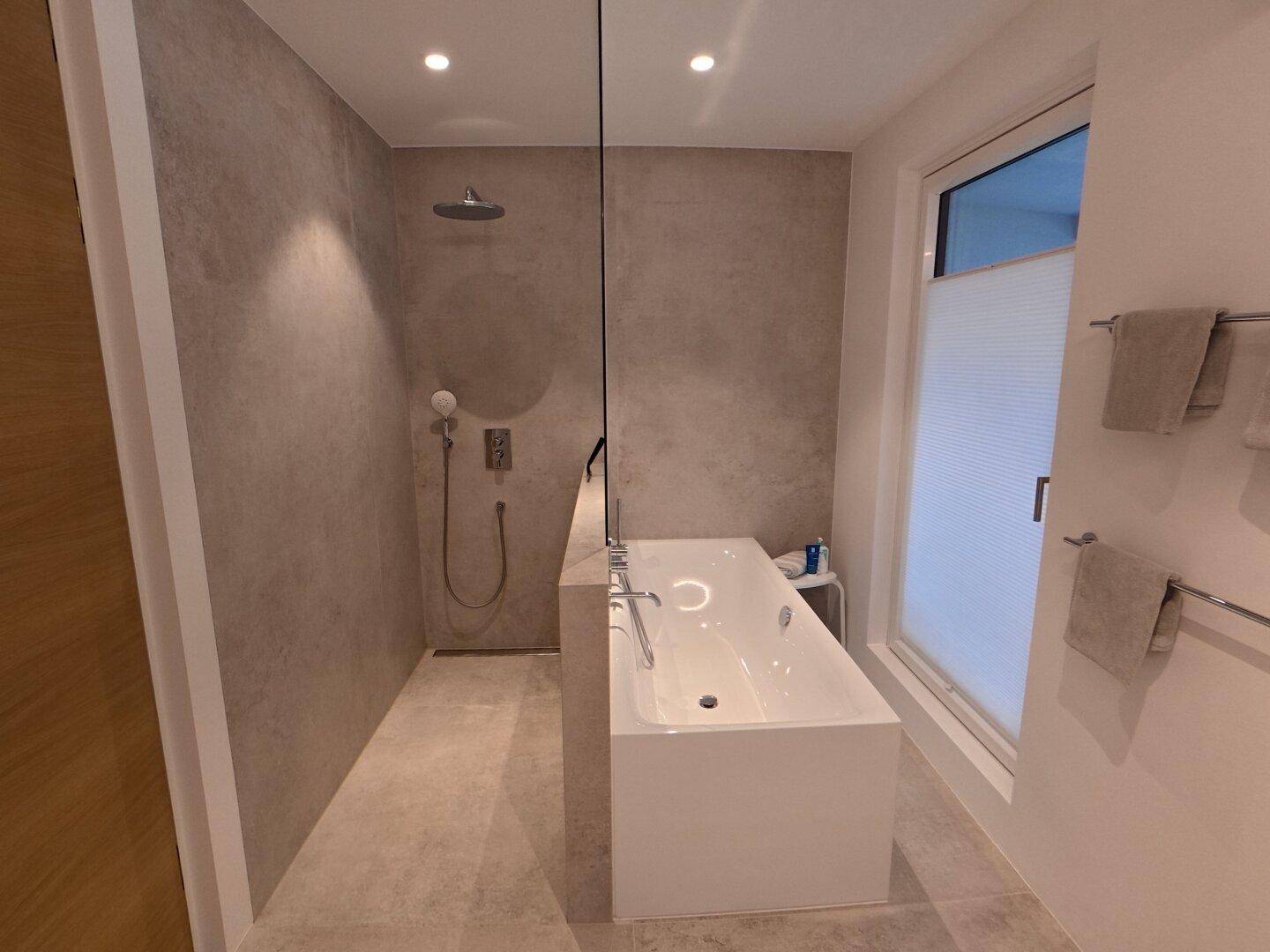 Modernes Badezimmer mit Badewanne, begehbarer Dusche und großformatigen Fliesen.