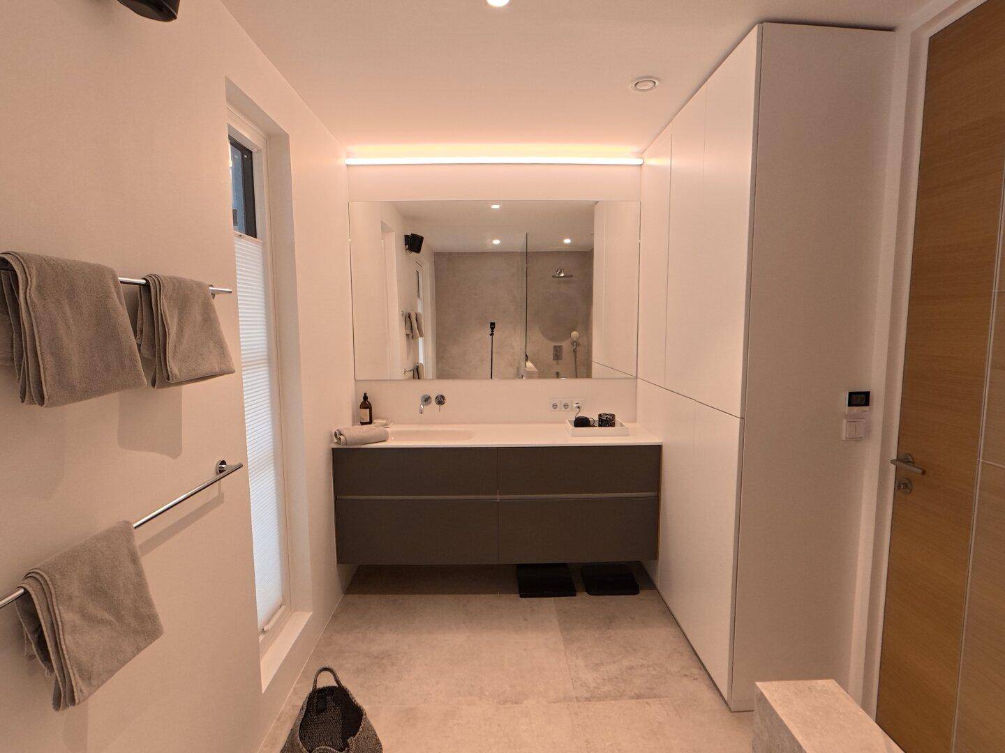 Elegantes Badezimmer mit Doppelwaschbecken, großem Spiegel und integrierten Schränken.