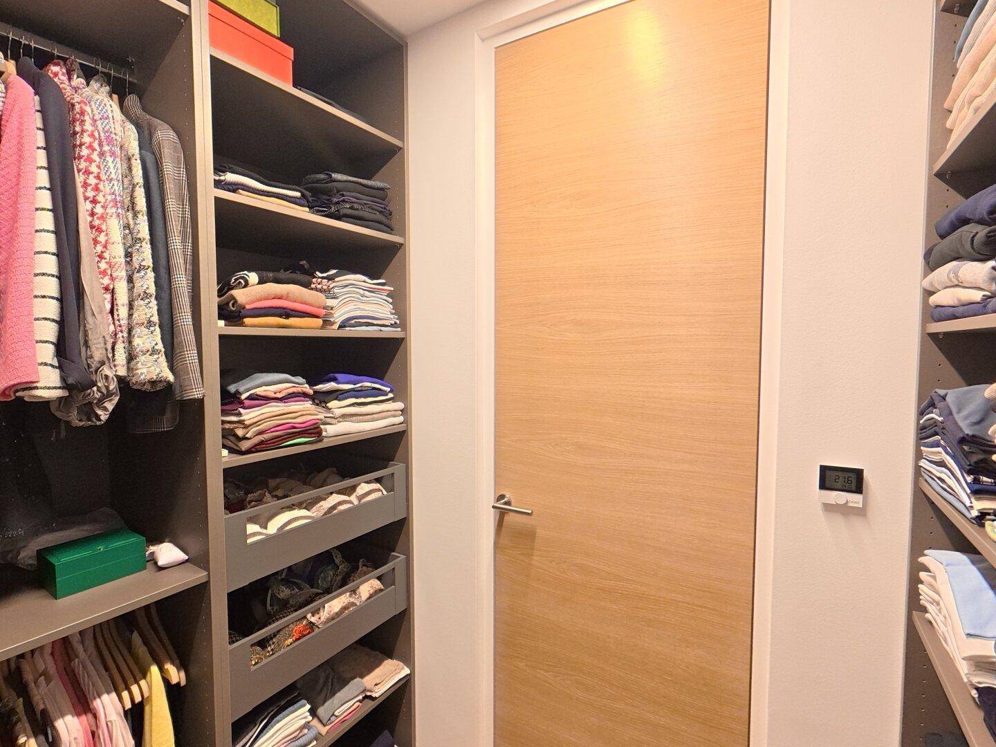 Begehbarer Kleiderschrank mit maßgefertigten Regalsystemen und Holztür.