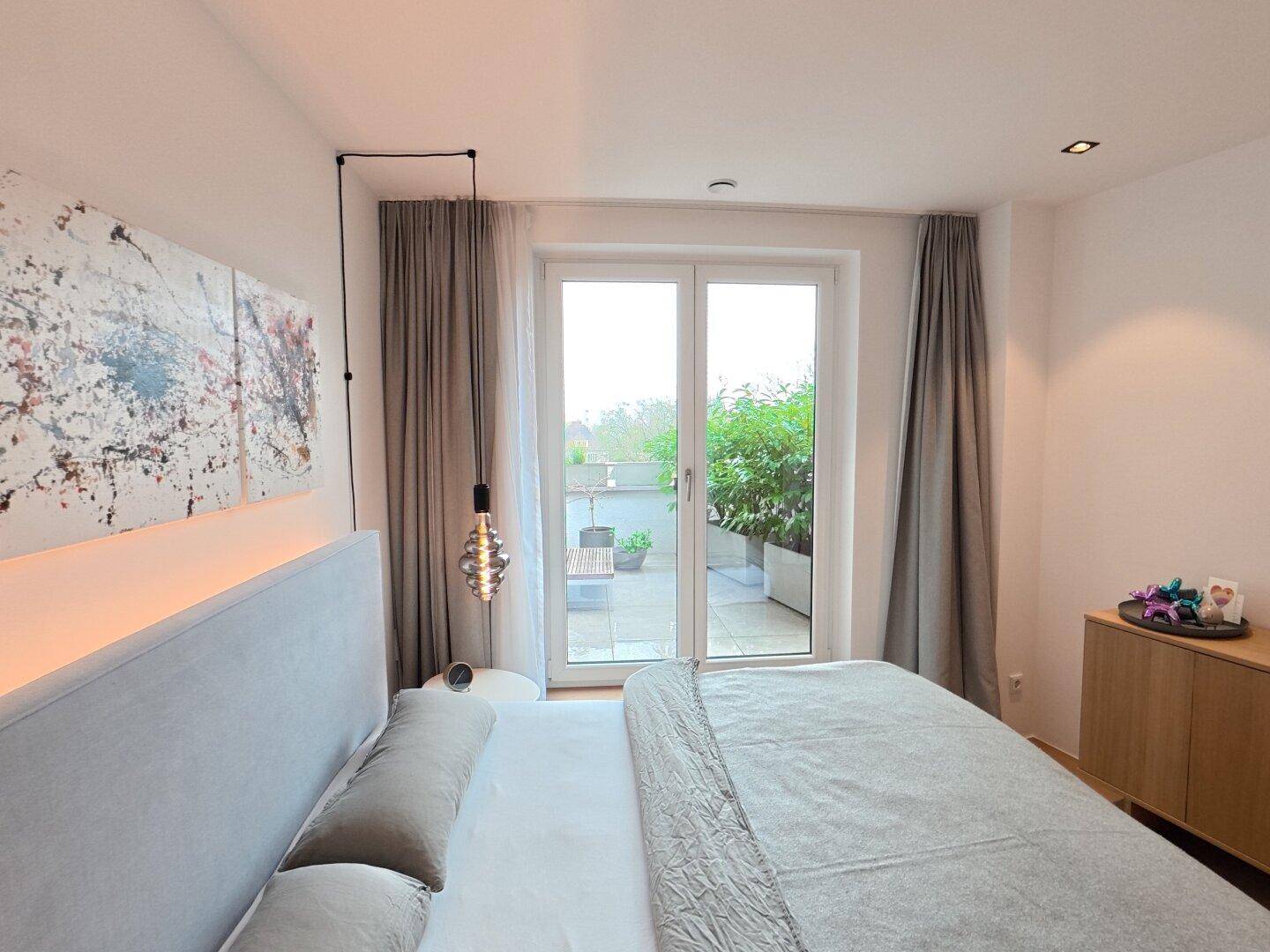 Schlafzimmer mit großem Fenster, Holzboden und Blick auf die Außenterrasse.
