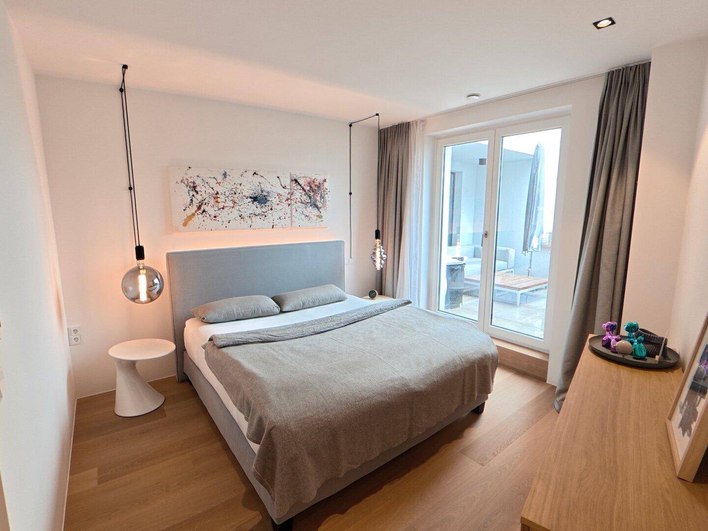 Helles Schlafzimmer mit Doppelbett, Holzboden und Zugang zu einer Außenterrasse.