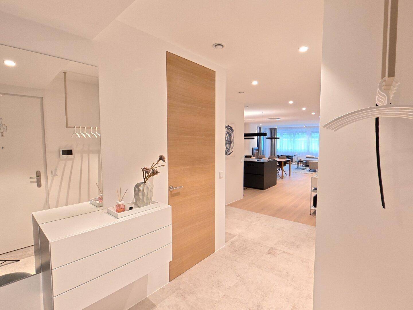 Heller Eingangsbereich mit modernem Spiegel, Garderobe und hellem Fliesenboden.