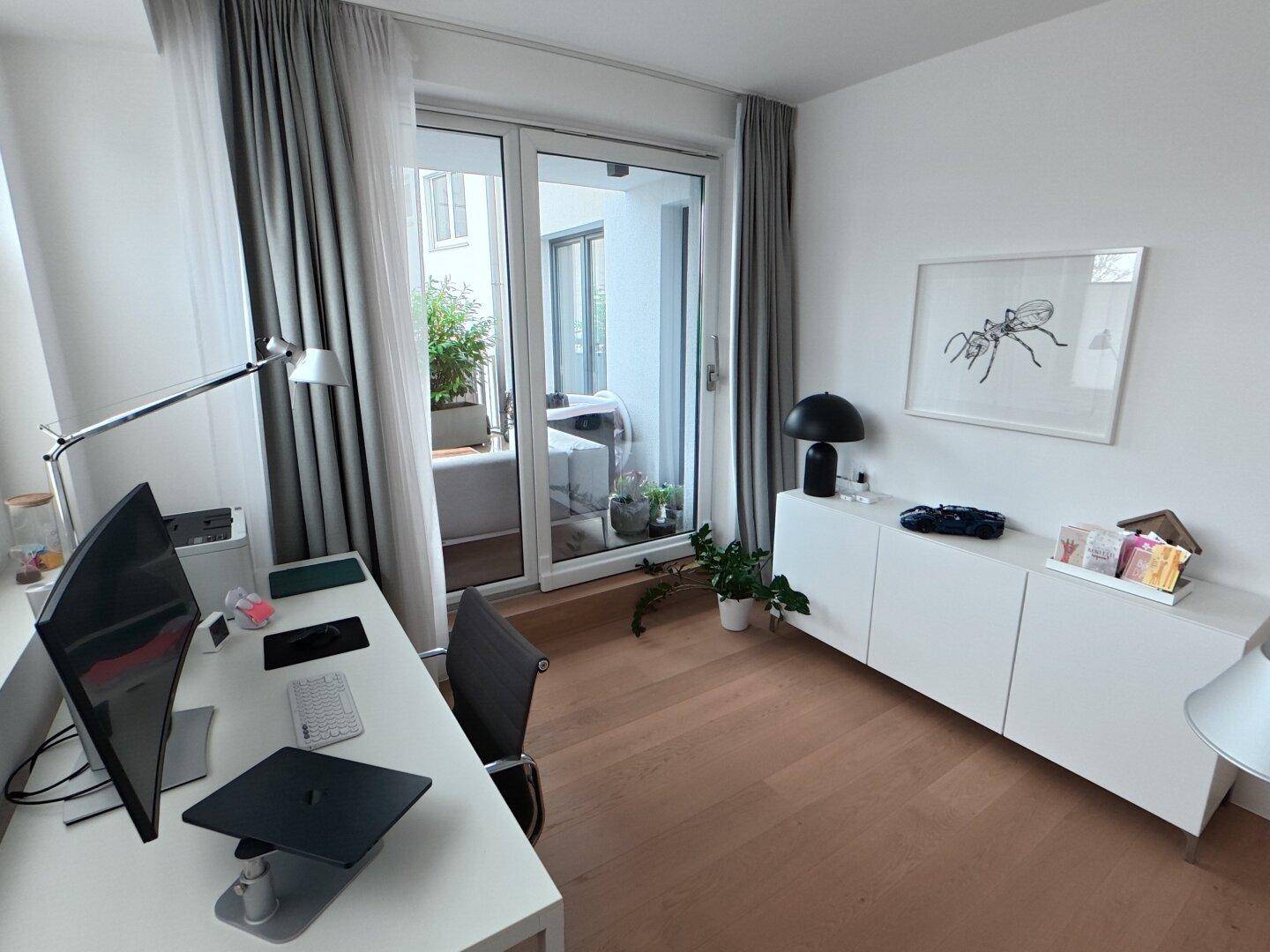 Arbeitszimmer mit Schreibtisch, Sideboard und Zugang zu einem Balkon oder einer Terrasse.