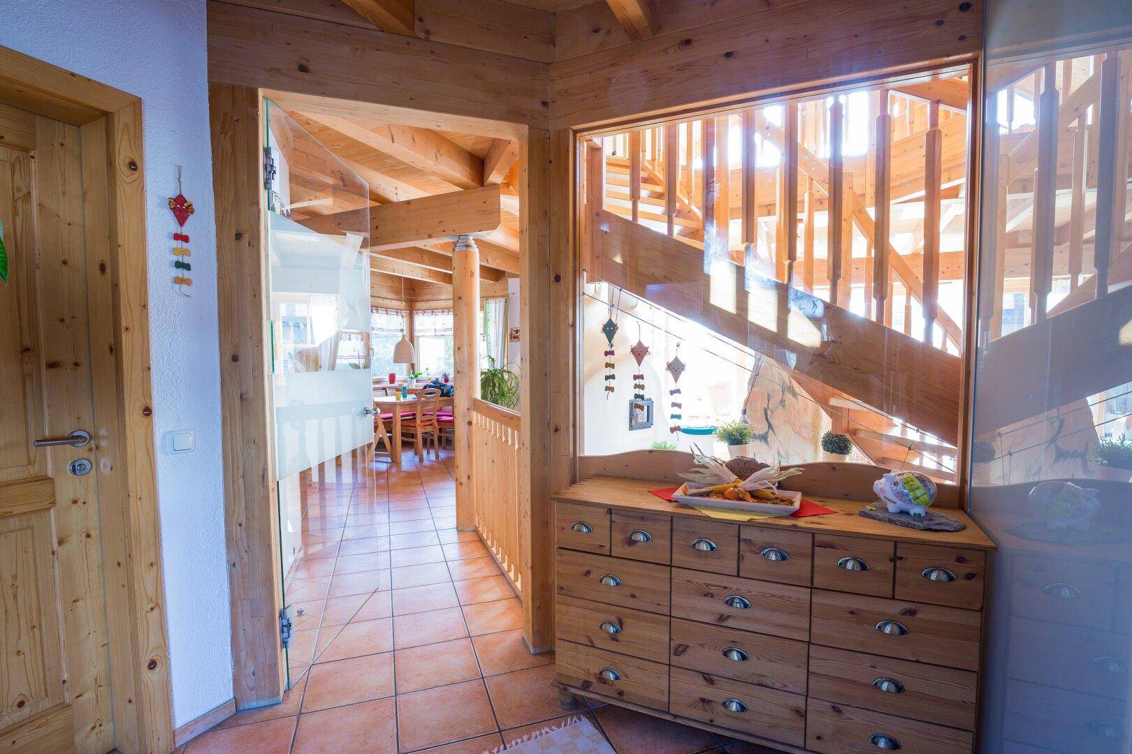 Flur mit Holzkommode und Blick auf die offene Holztreppe, die das Haus verbindet.