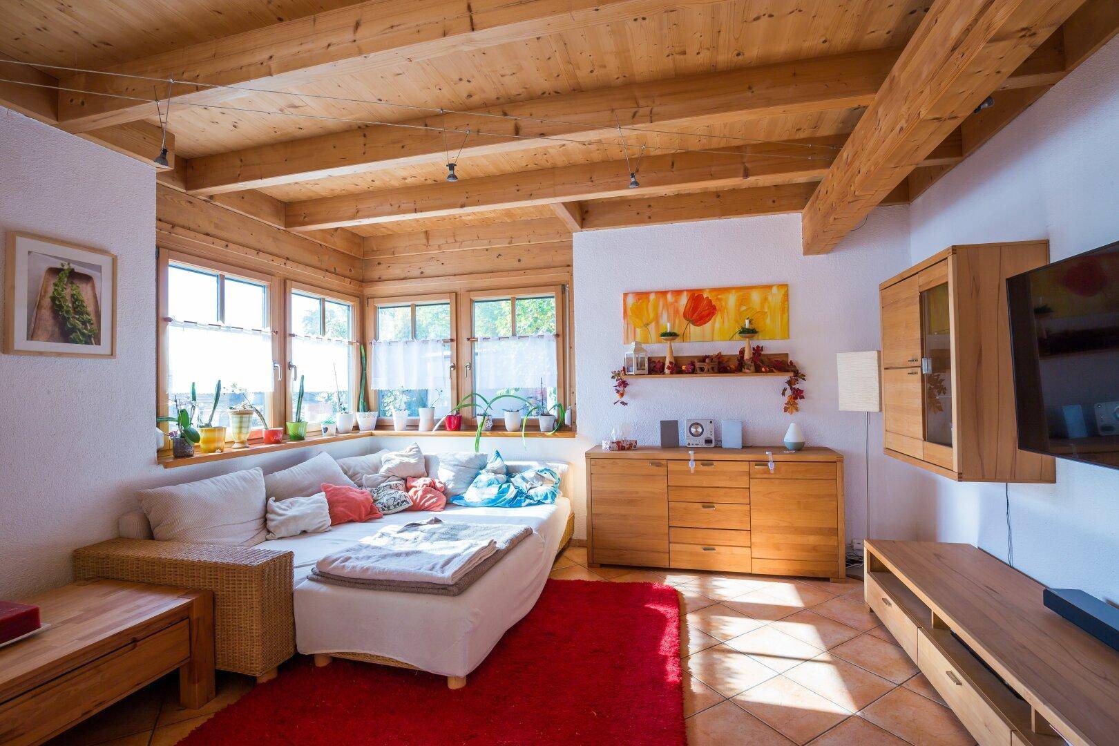 Helles Wohnzimmer mit Holzbalkendecke, bequemer Couch und großen Fenstern, die viel Tageslicht hereinlassen.