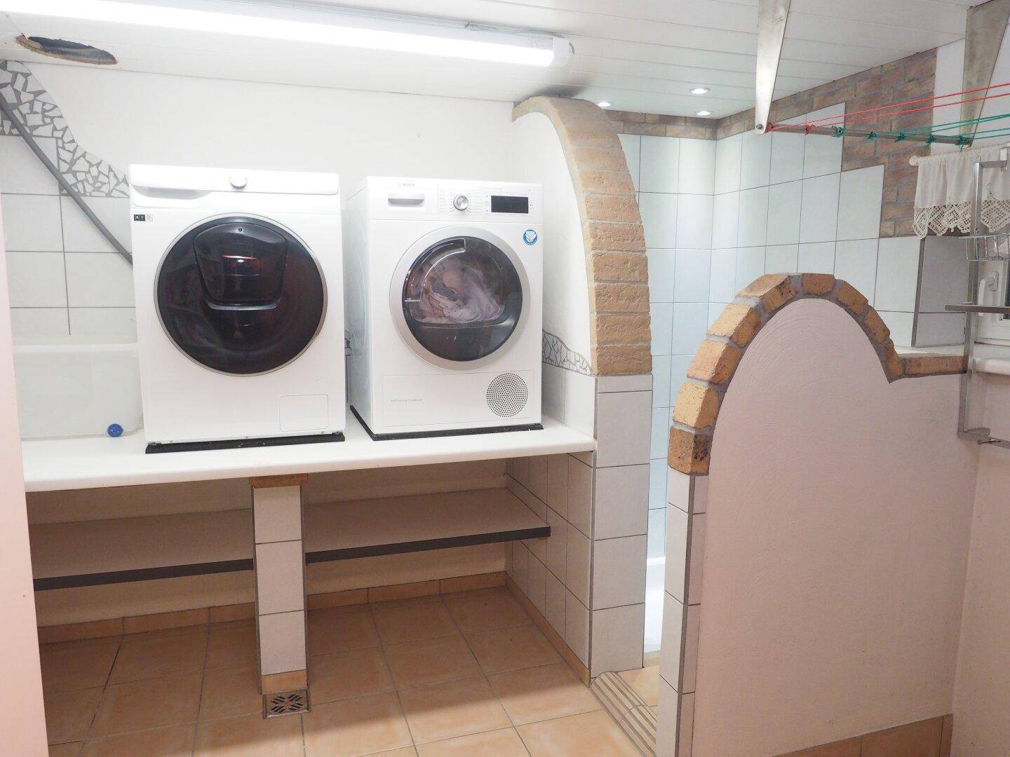 Praktischer Waschraum im Keller mit Waschmaschine, Trockner und Fliesenboden.