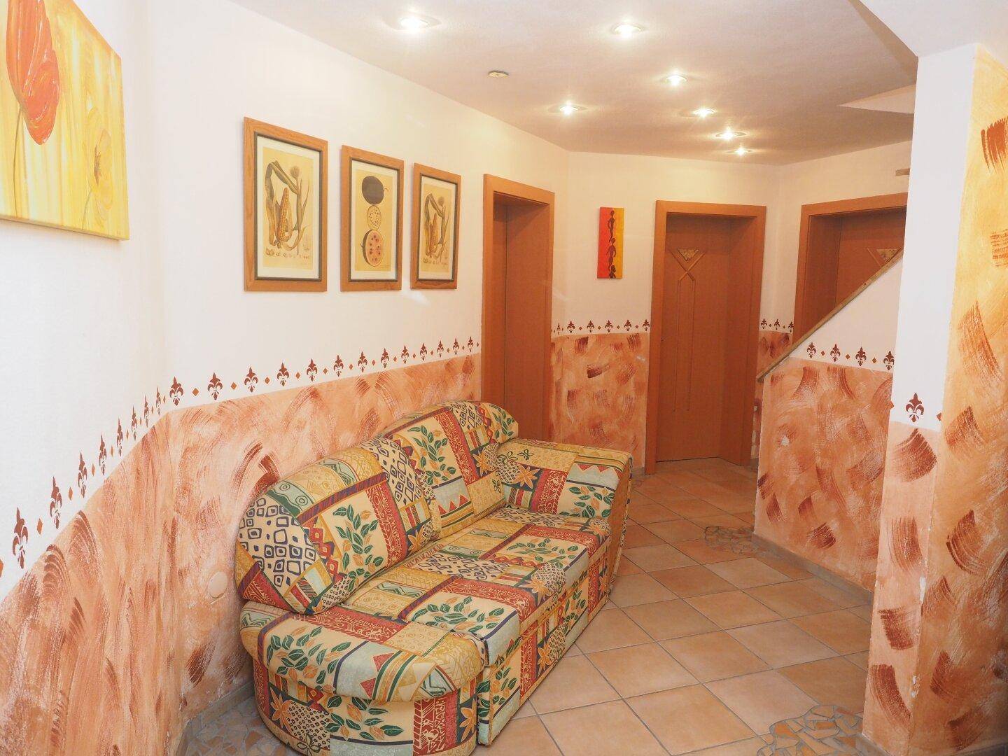 Heller Kellerraum mit bequemer Couch, Terrakottafliesen und dekorativen Wandmalereien.