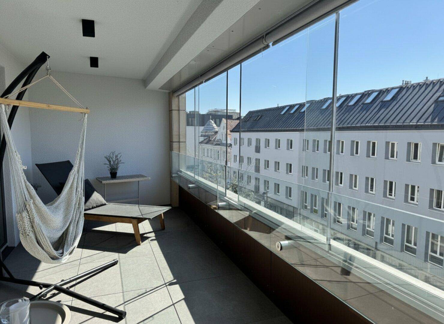 Verglaster Balkon mit Hängematte und Blick auf die umliegenden Gebäude.