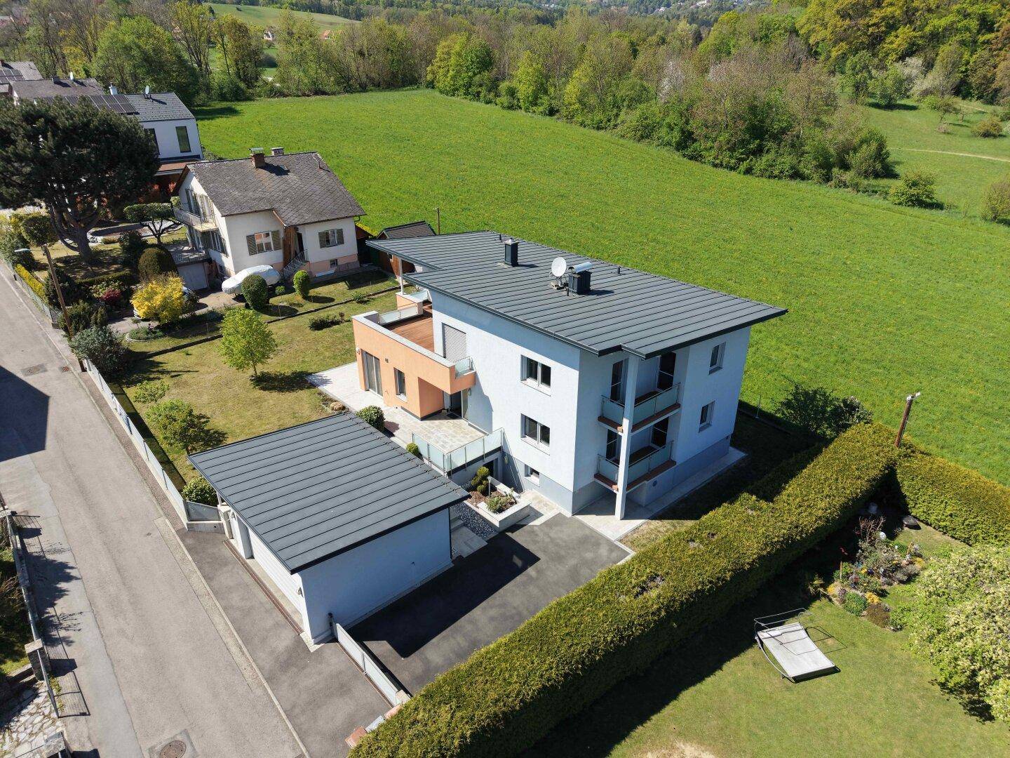 Vogelperspektive eines modernen Hauses mit Flachdach, Garage und weitläufigen Grünflächen in der Umgebung.