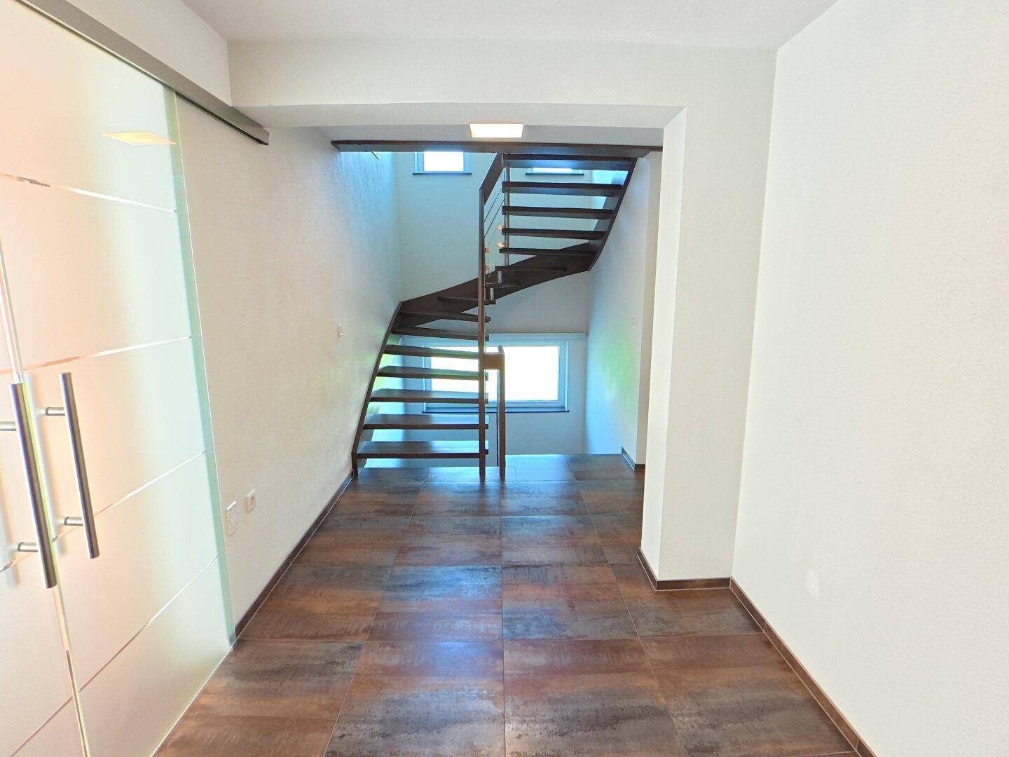 Heller Flur mit moderner Holztreppe und Fliesenboden, der zu den oberen Etagen führt.