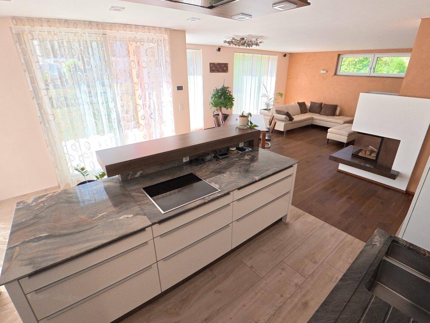 Offener Wohnbereich mit moderner Küche, Essbereich und Kamin, durchflutet von Tageslicht.