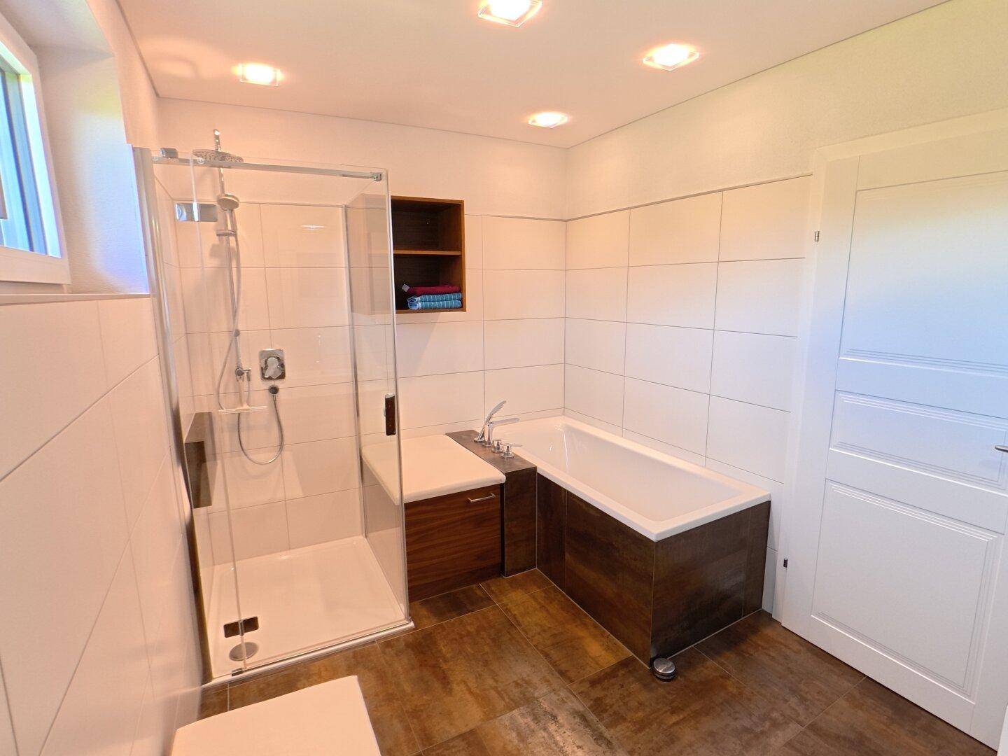 Modernes Badezimmer mit Badewanne, Glasdusche und Fliesenboden in warmen Farbtönen.
