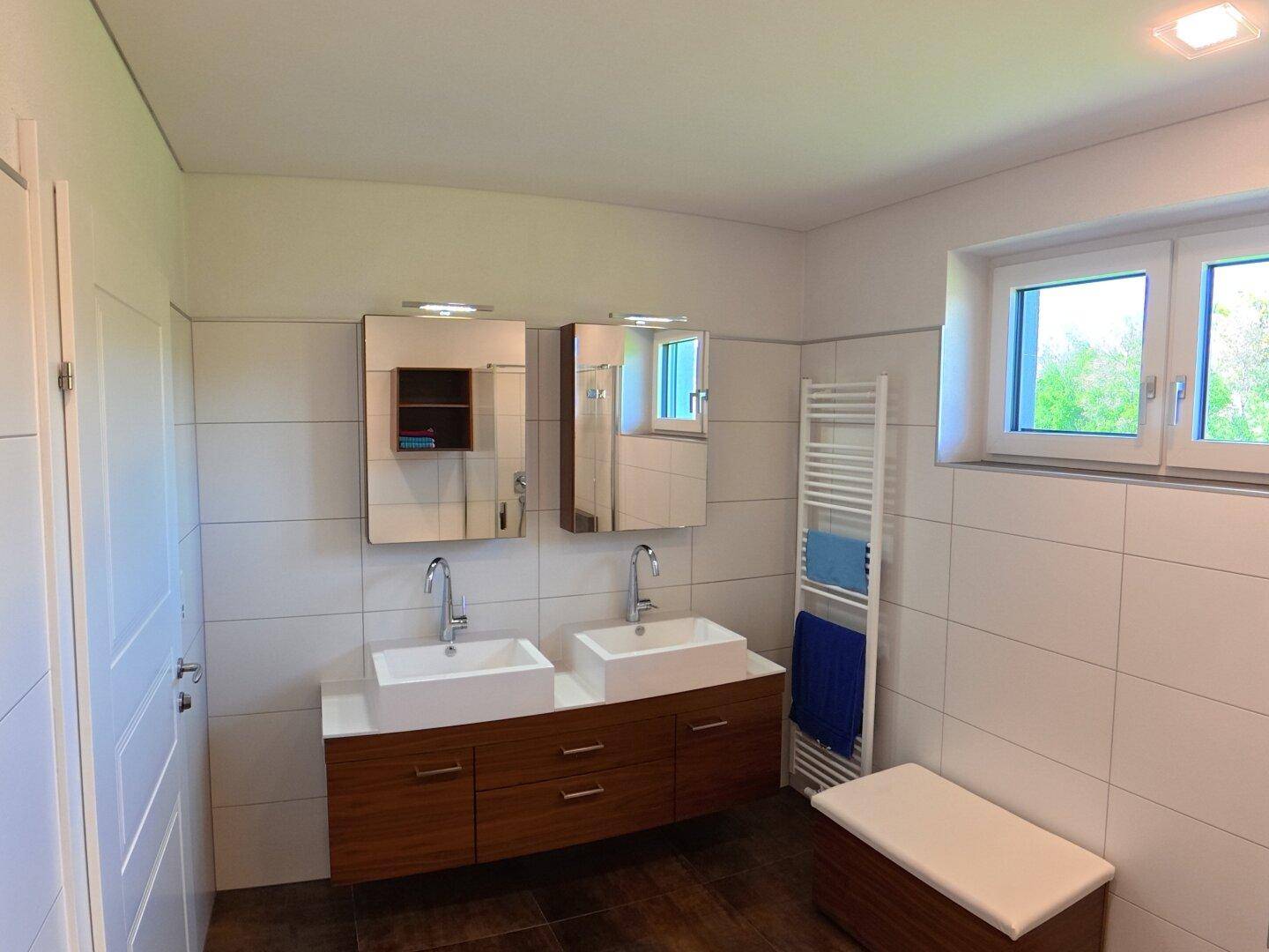 Geräumiges Badezimmer mit Doppelwaschbecken, Spiegelschränken und beheiztem Handtuchhalter.