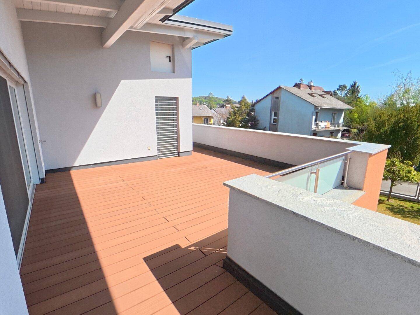 Große Holzterrasse mit Glasgeländer und Blick auf die umliegende Wohngegend.