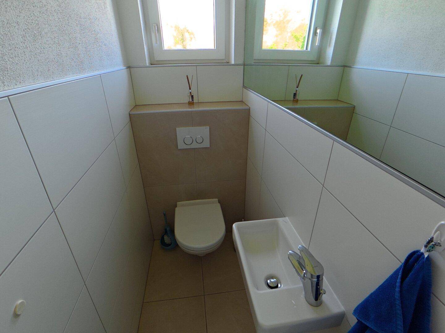 Helles Gäste-WC mit modernem Wand-WC, kleinem Waschbecken und Fenster für Tageslicht.