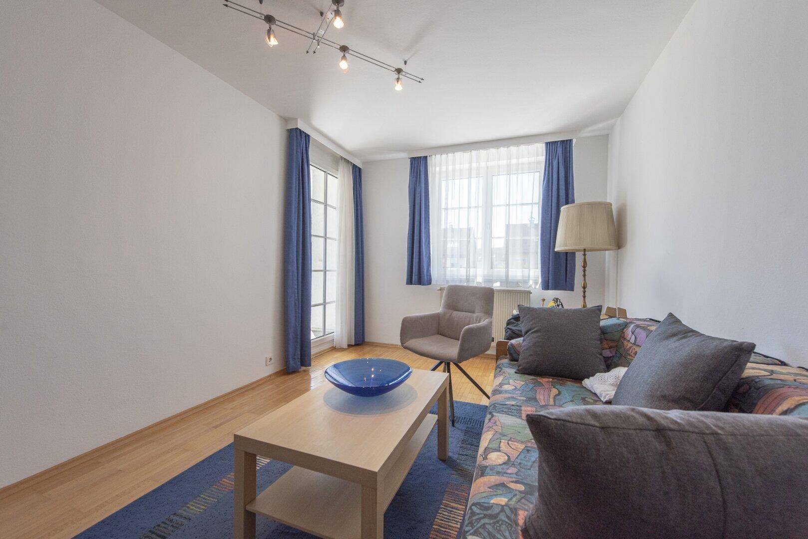 Gemütlicher Wohnraum mit Holzboden, Sofa und blauen Vorhängen, hell und einladend.
